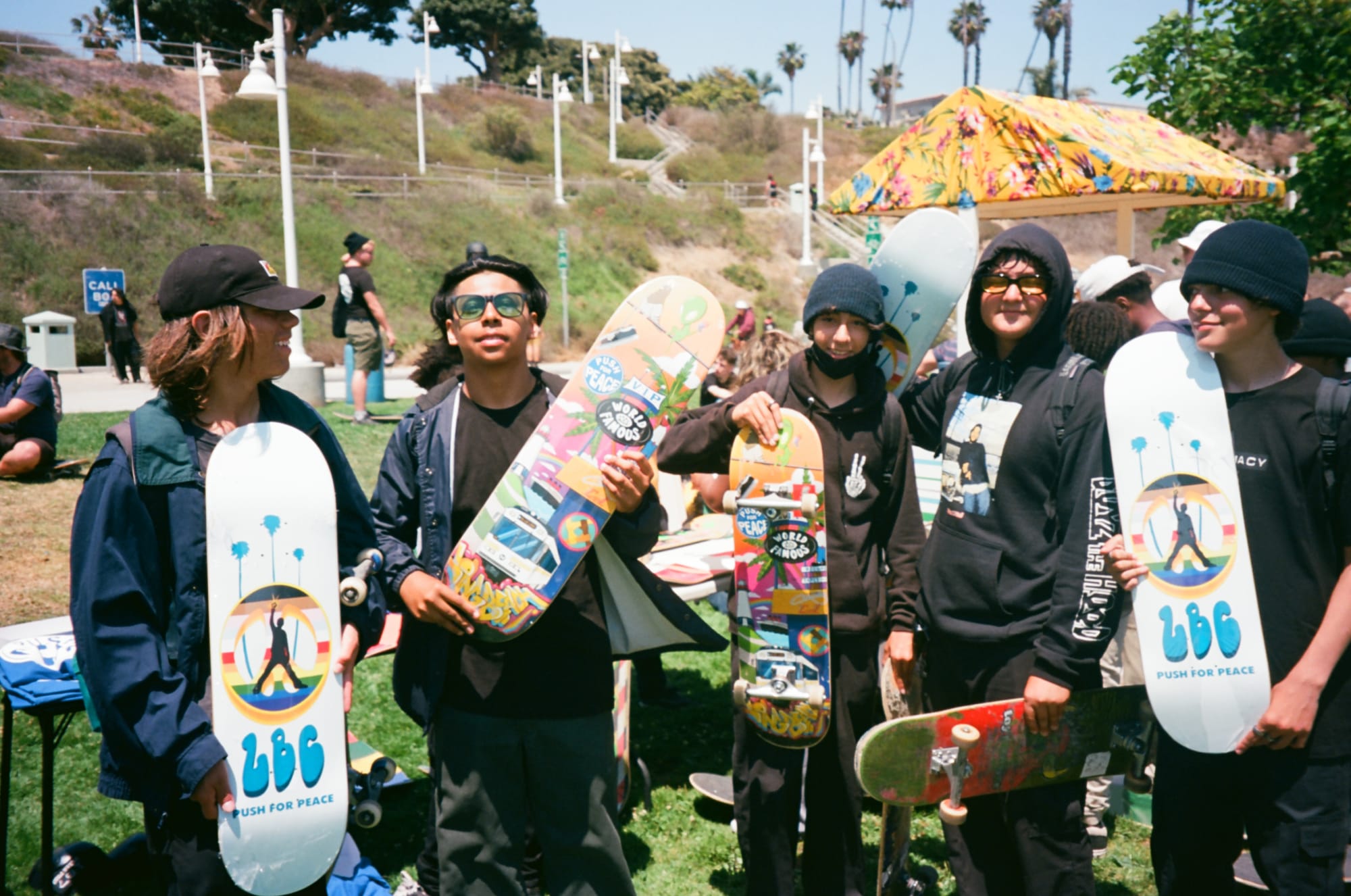 Five young skateboarders wearing jackets, hoods, hats and beanies hold up new skateboards with colorful designs.