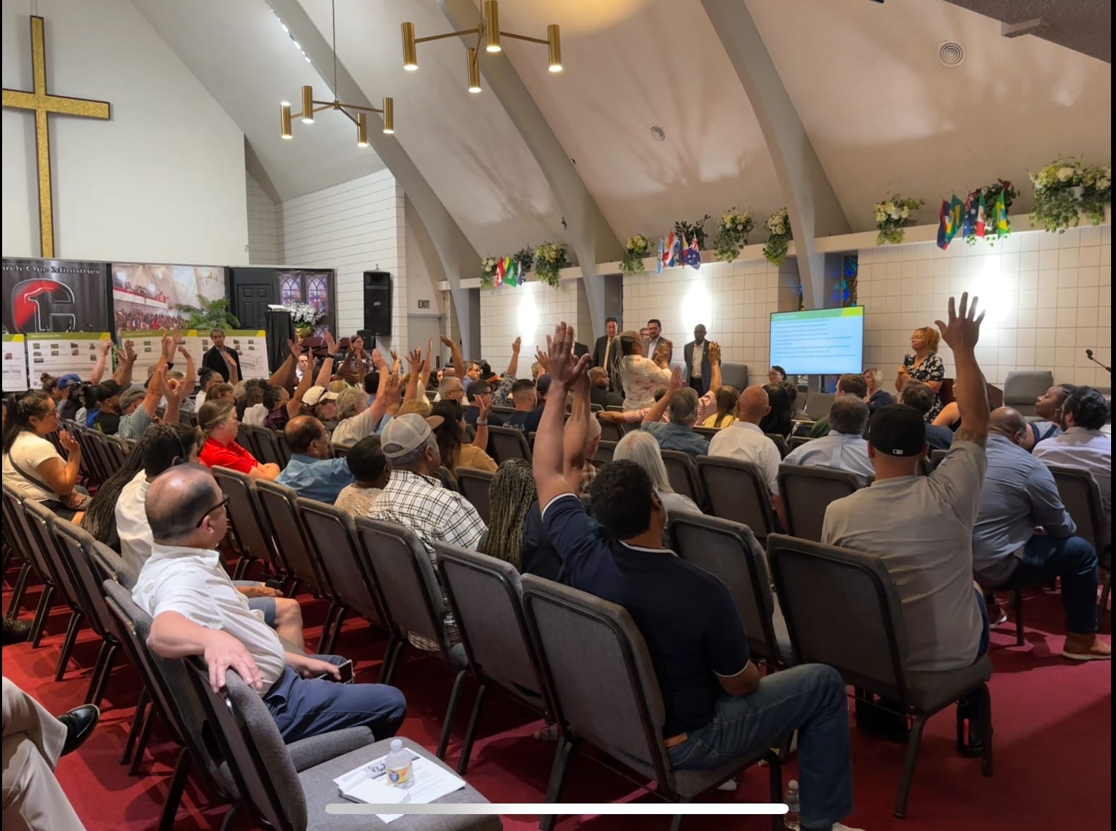 A few dozen people sit in gray chairs while many raise their arms.