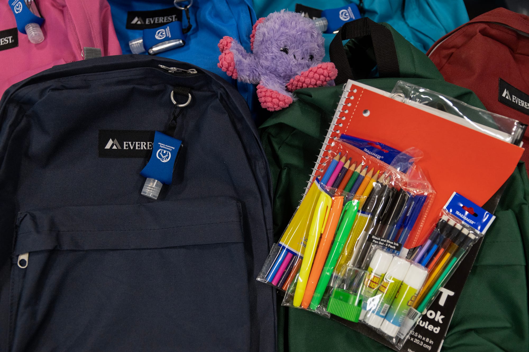 Notebooks, pencils, markers and other school supplies sit on blue, green, pink, red and other backpacks.