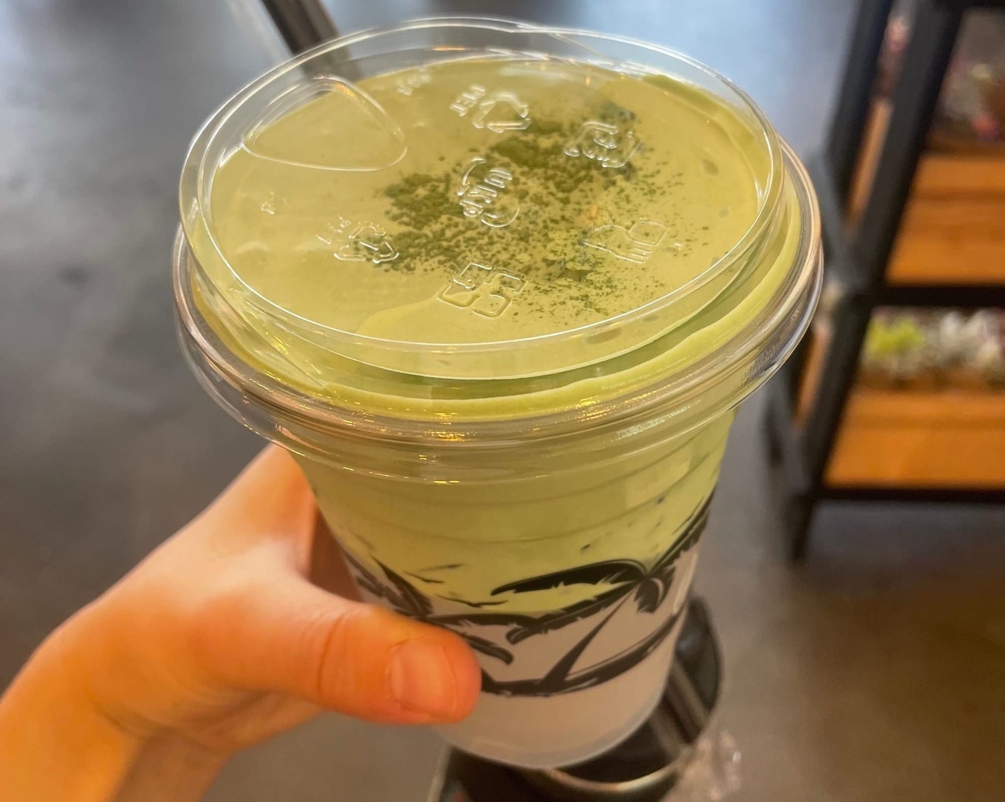 A hand holding a partly green beverage in a plastic cup with lid.