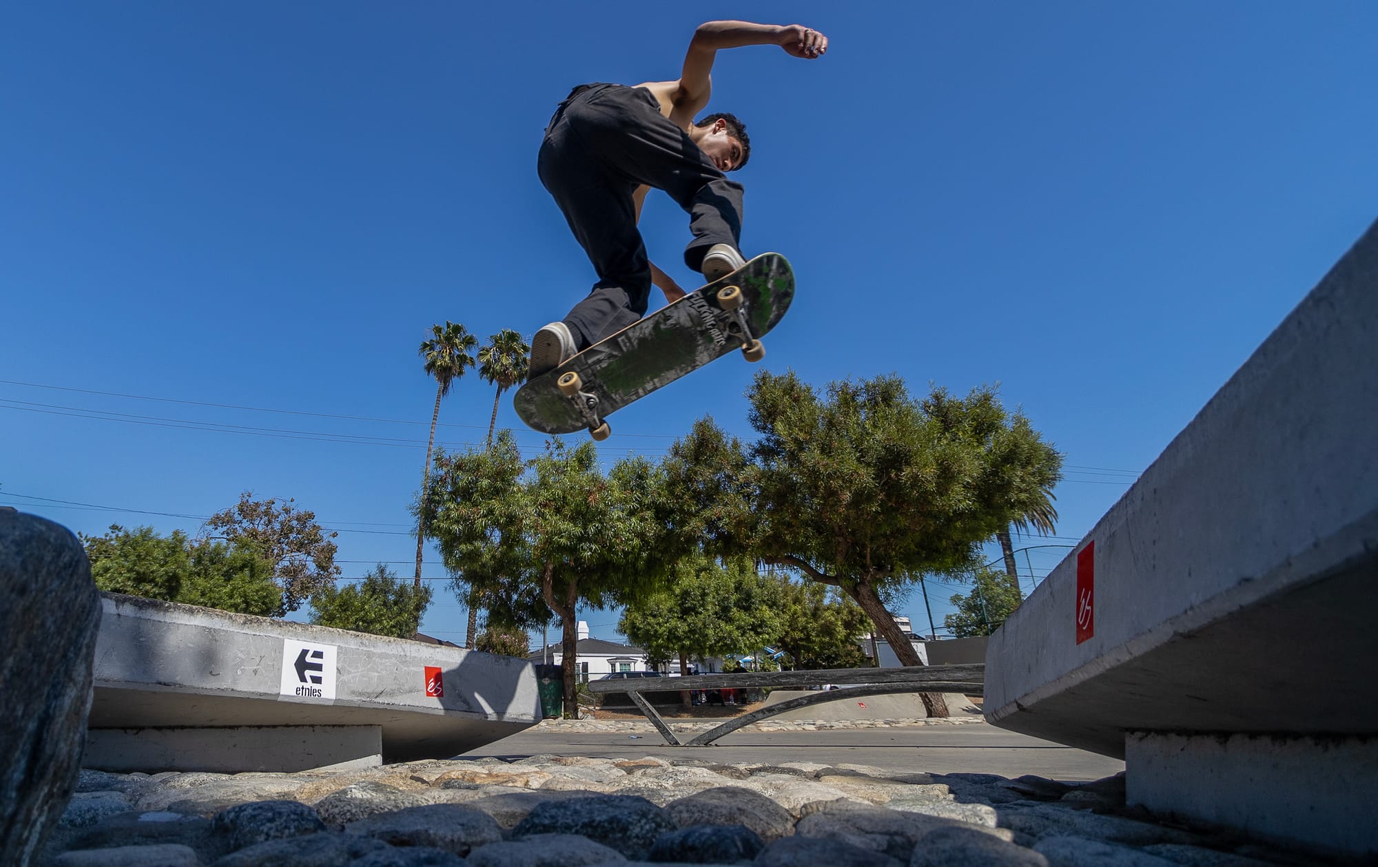 A young person wearing dark pants and no shirt flies through the air on a skateboard.