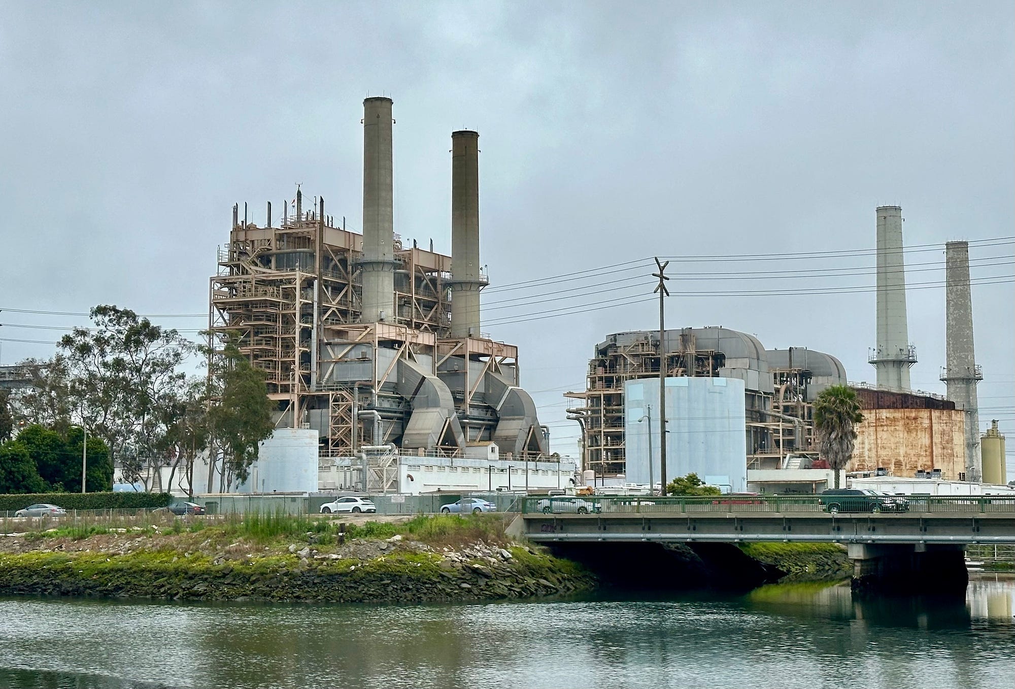 Gray power plant with four cylindrical smokestacks sits next to a river.