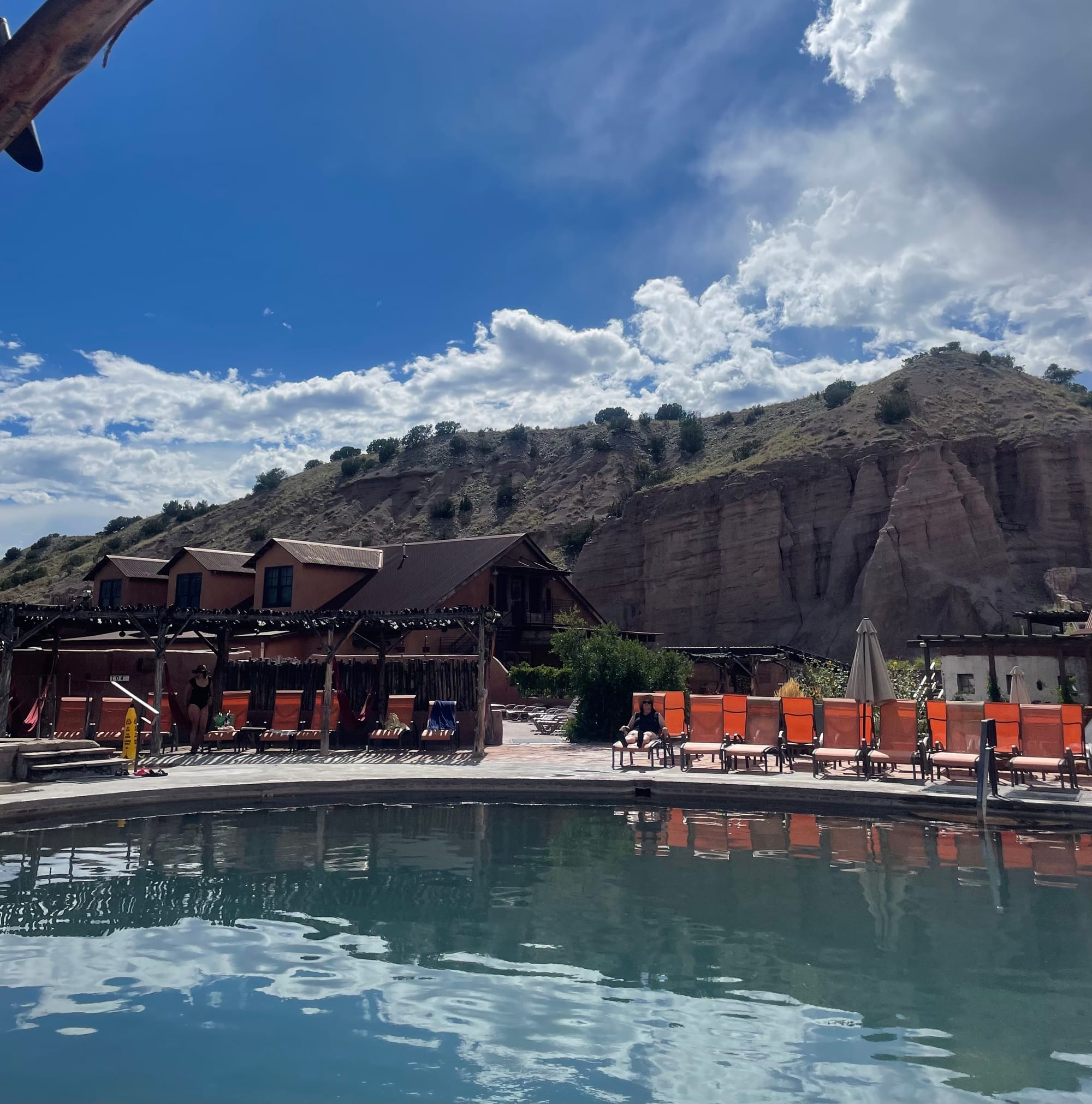 Orange chairs lined up next to a pool, situated near a rocky cliff. 