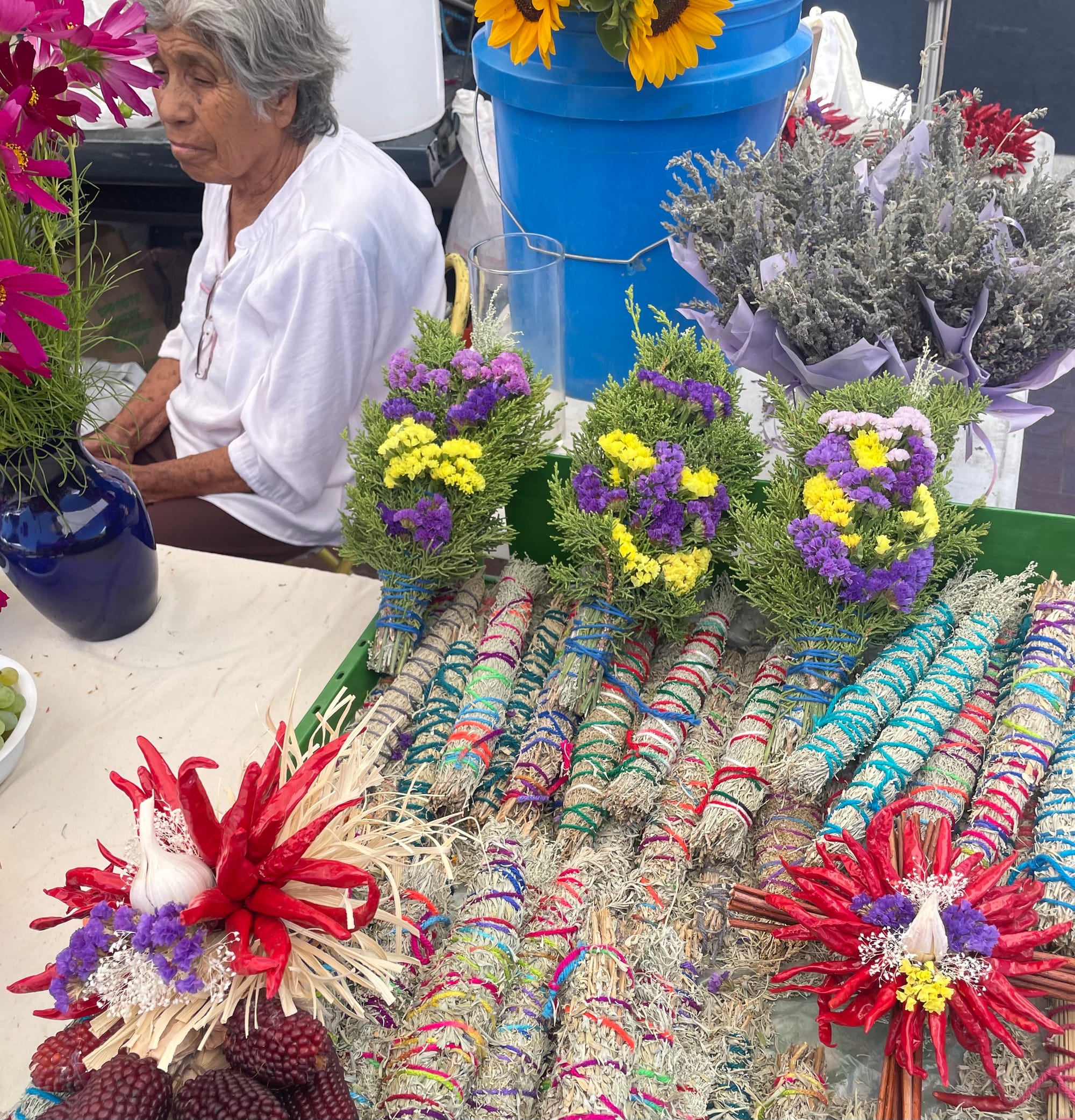 Woman sits a table covered with flowers and flower arrangements.