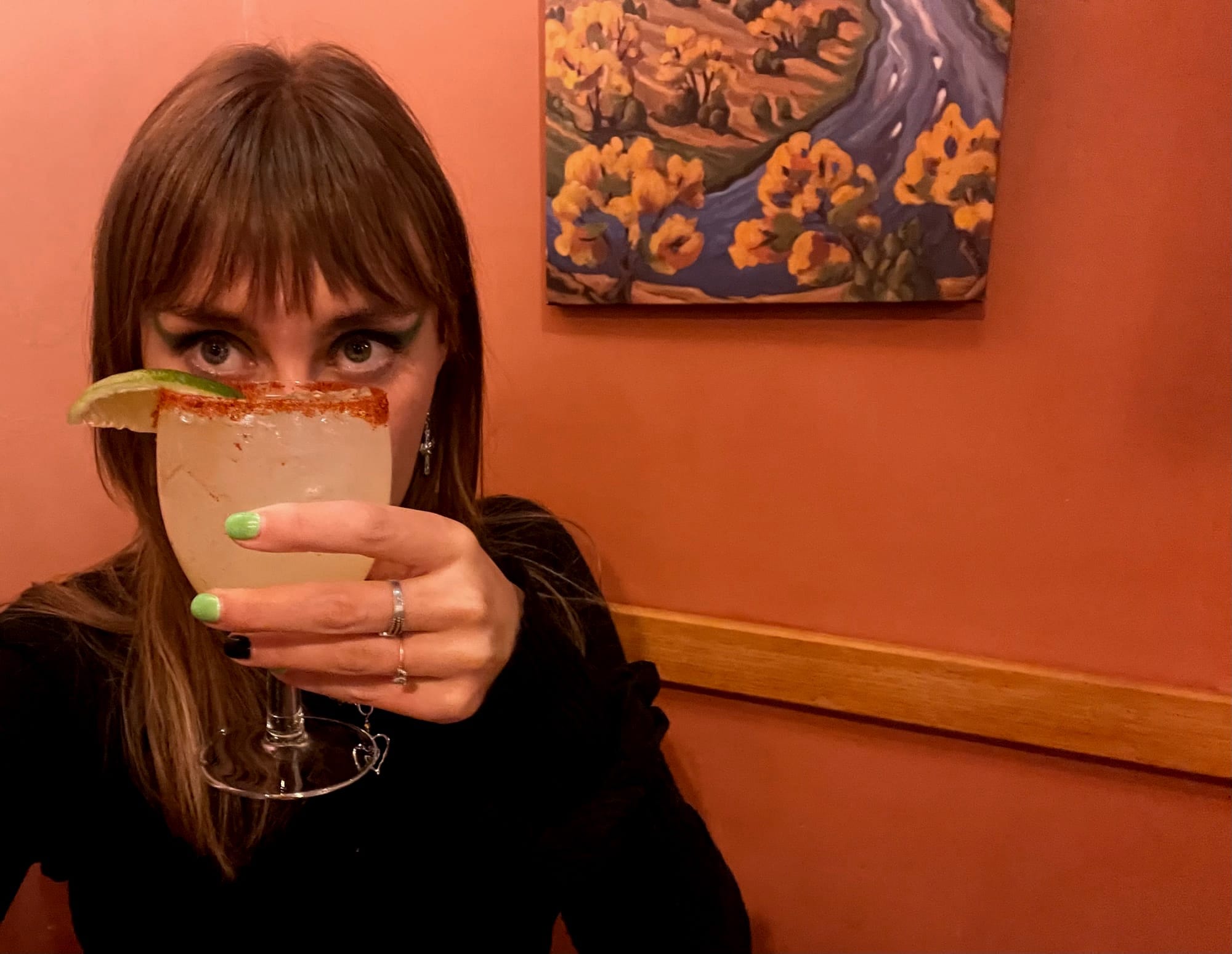 Woman holding a margarita in front of her face, obscuring all features but her eyes.