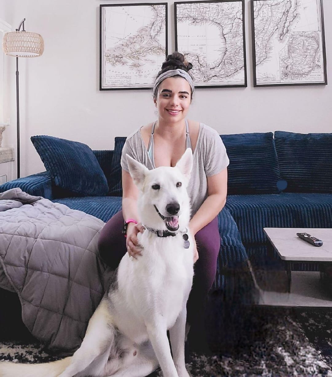 A woman sits on a blue couch while petting a large white dog.