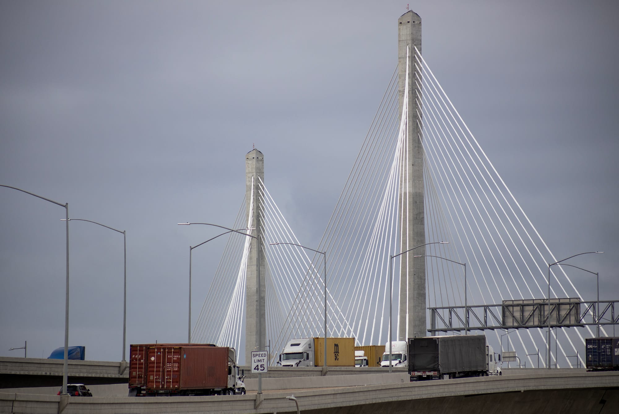 Trucks drive over gray and white suspension bridge.