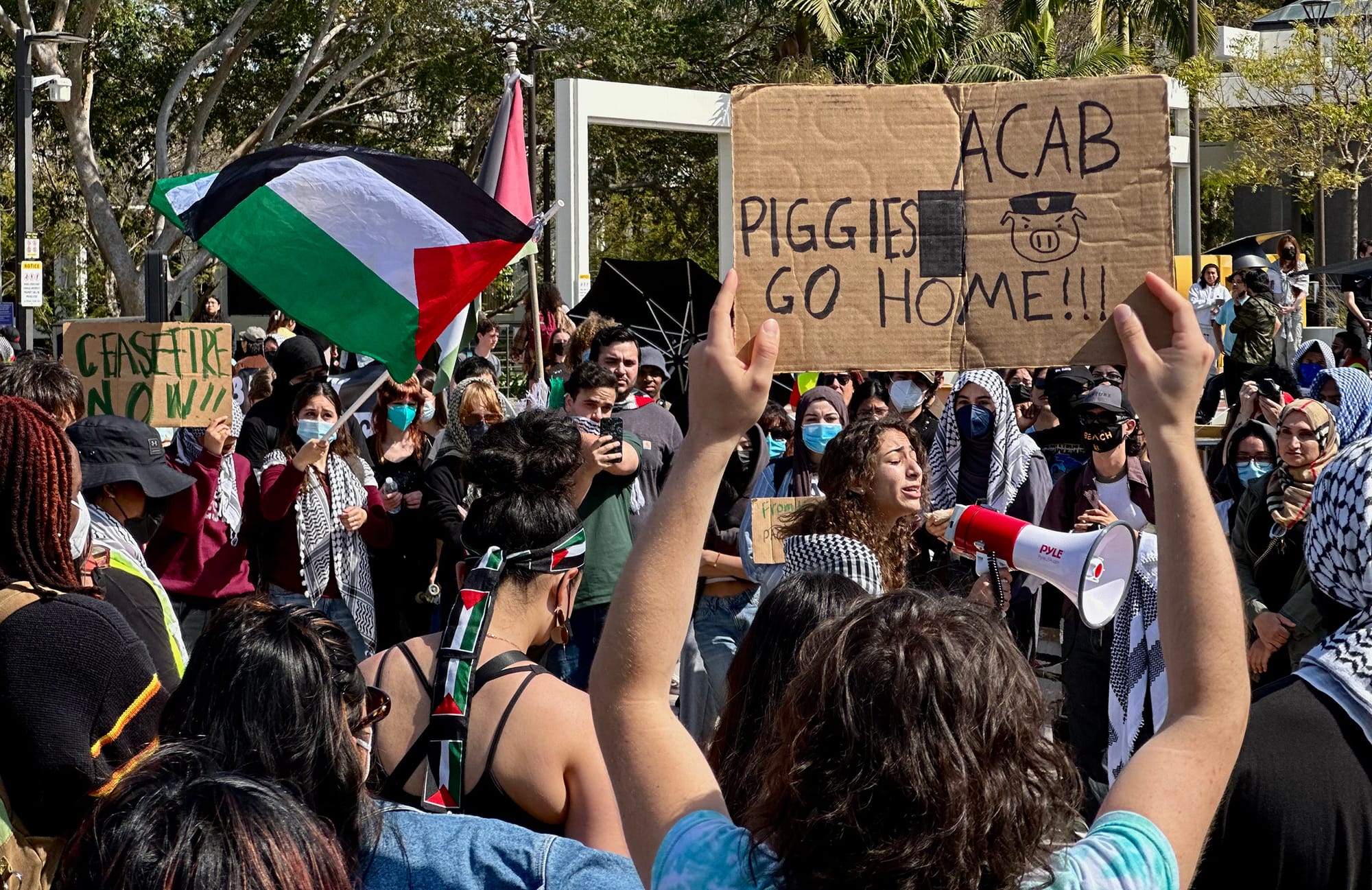 A young woman speaks into a bullhorn surrounded by protesters with signs and flags.