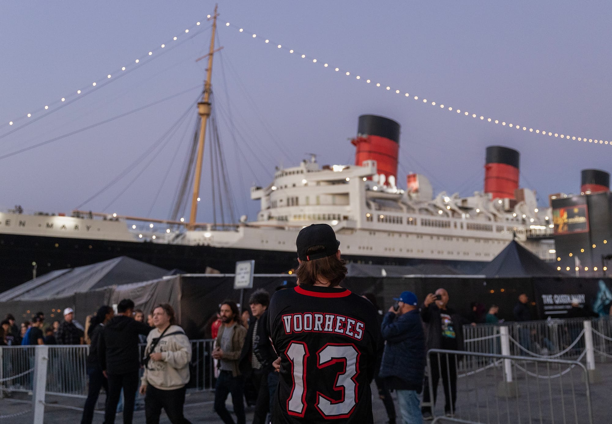 A man in a jersey that says "Vorhees 13" stands in front of the Queen Mary ocean liner.