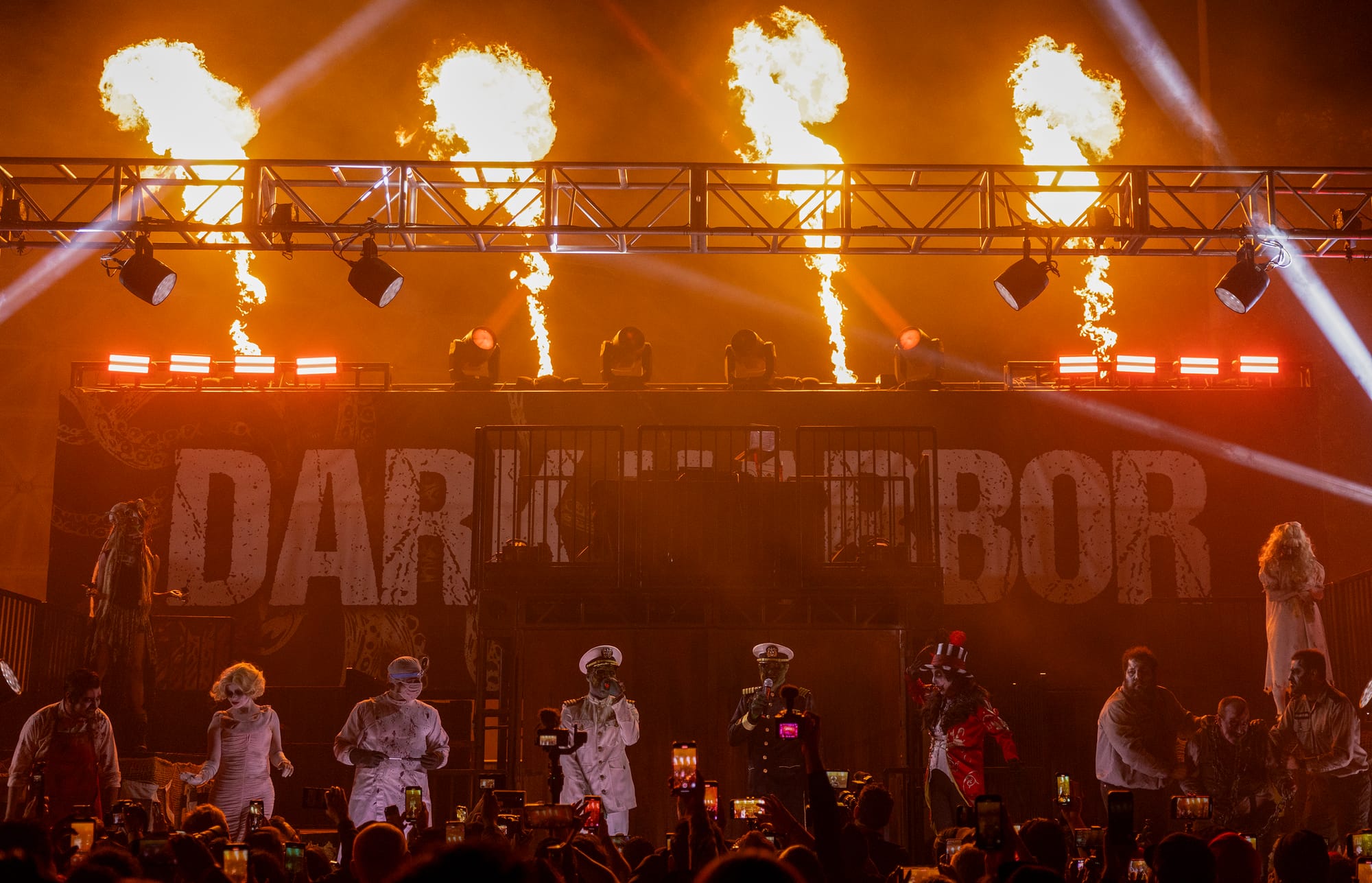 People in horror costumes stand on a stage while flames shoot up behind them.