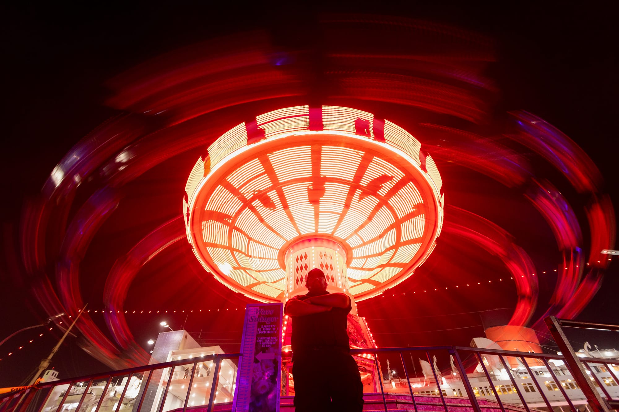 A man folds his arms across his chest in front of brightly lit swings.