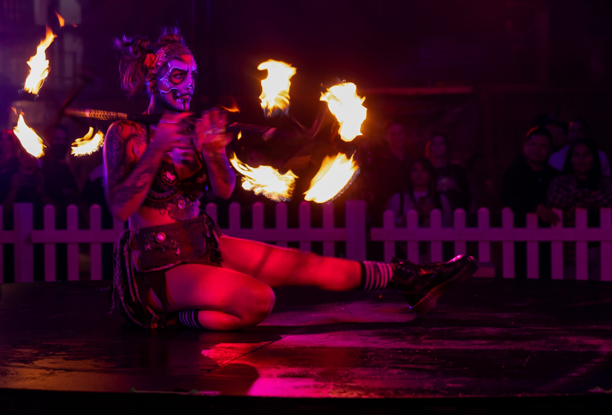 A person in heavy face makeup twirls fire as part of a performance.