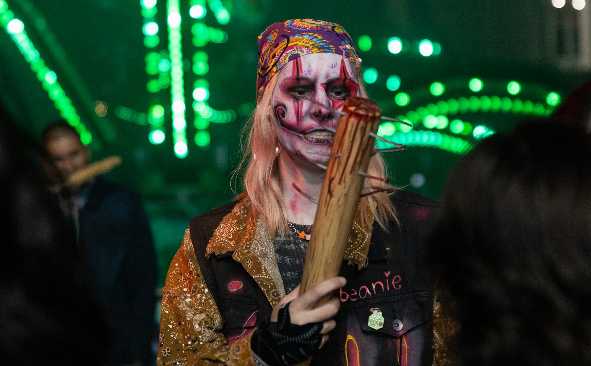 A person in heavy face paint holds a baseball bat with spikes in it.