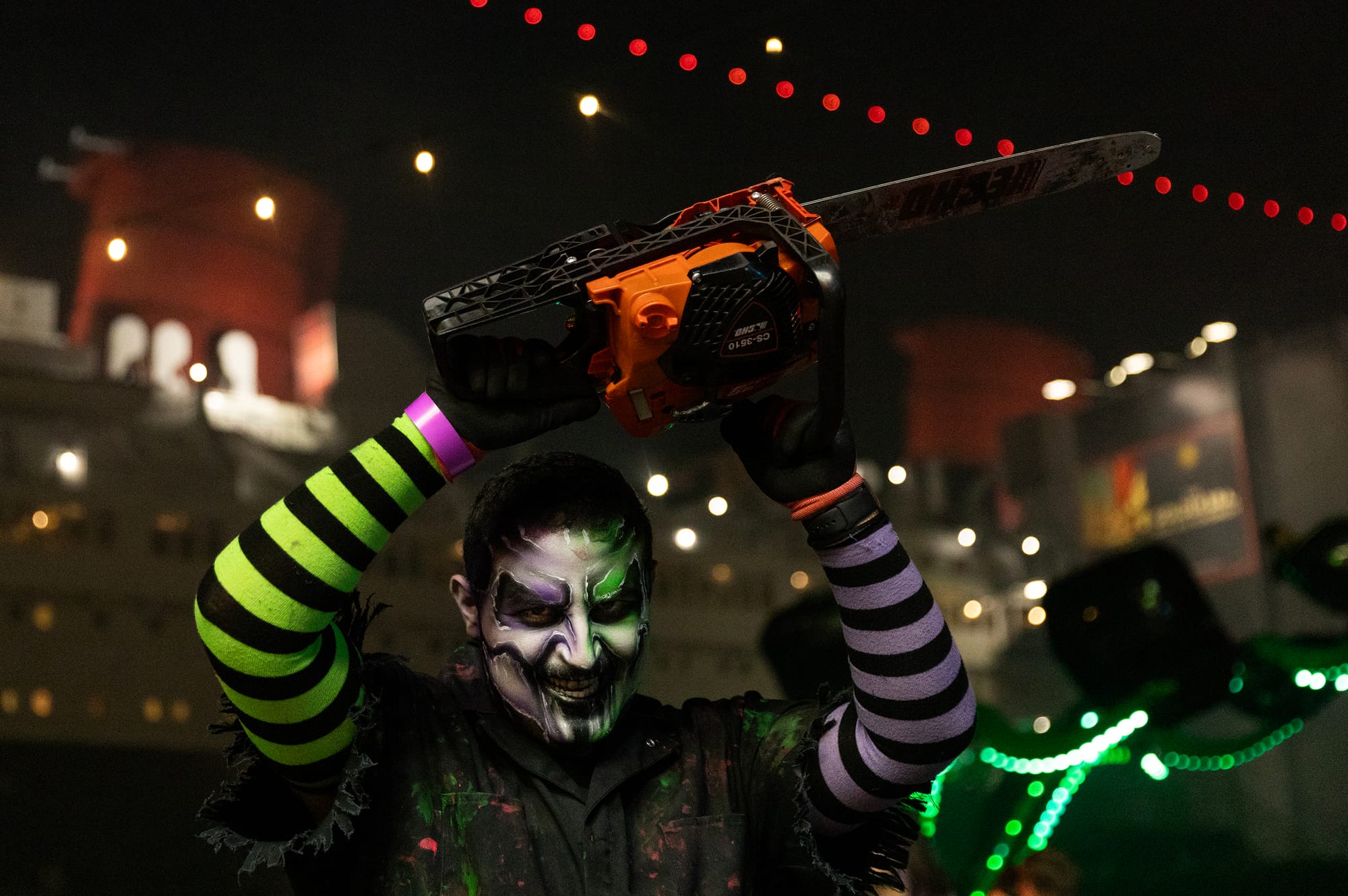 A person in scary makeup holds a chainsaw above their head.