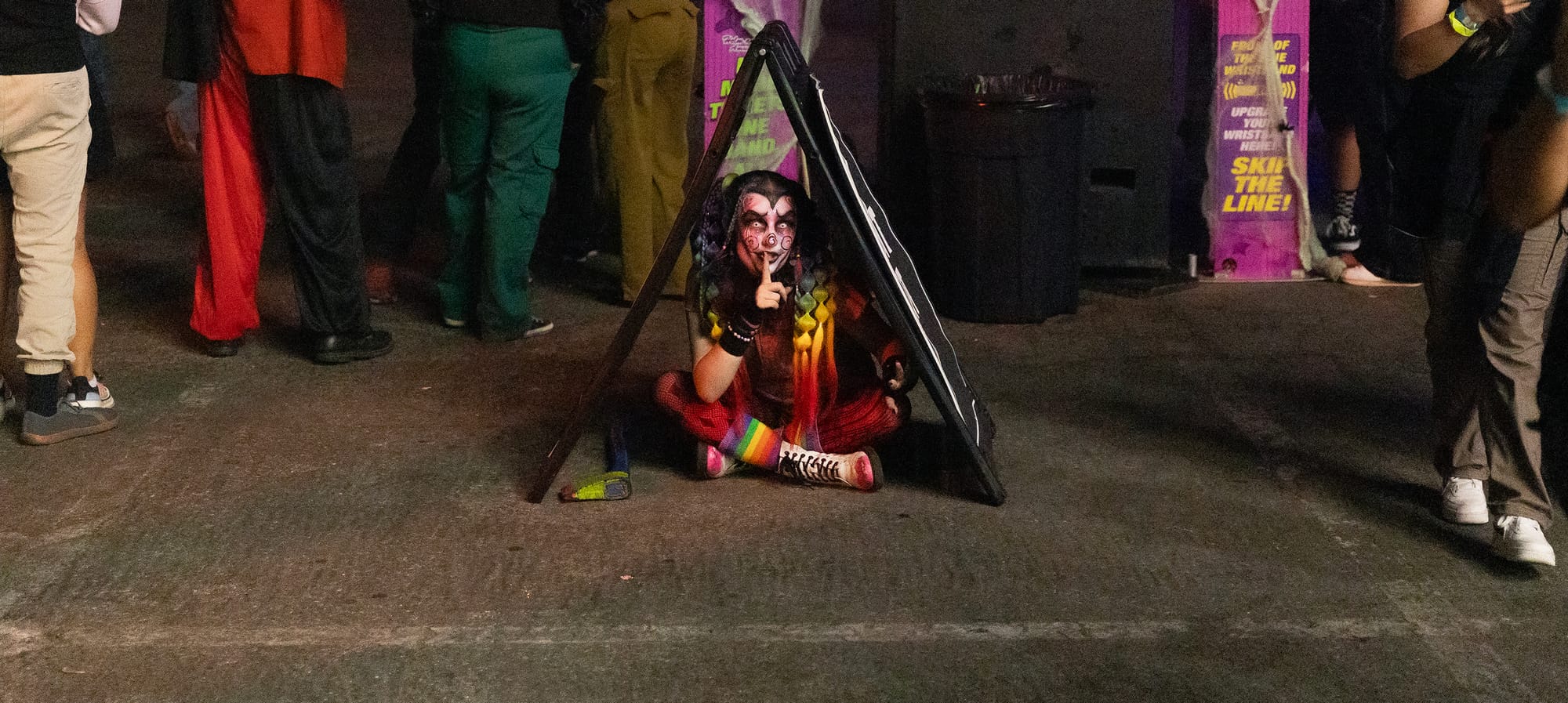 A person in heavy face paint sits cross-legged under a small A frame.