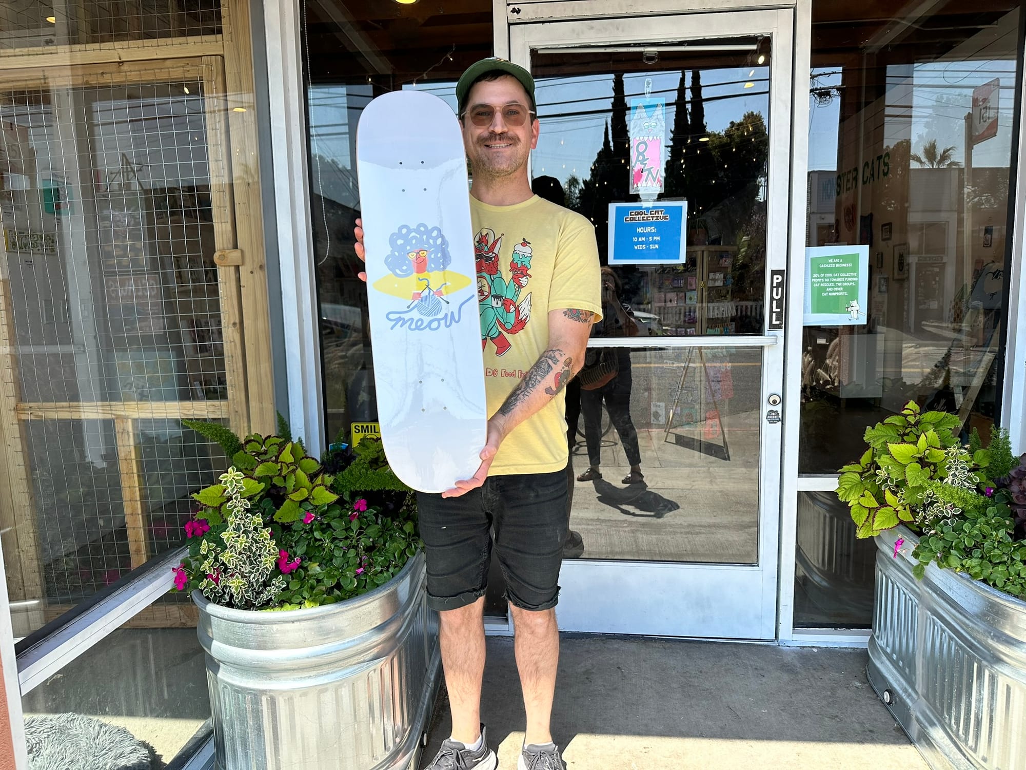 A man stands in front of a door holding up a skateboard.