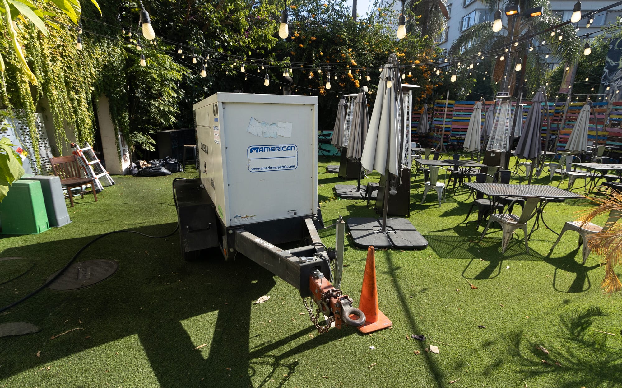 A large generator sits next to umbrellas on a restaurant patio.