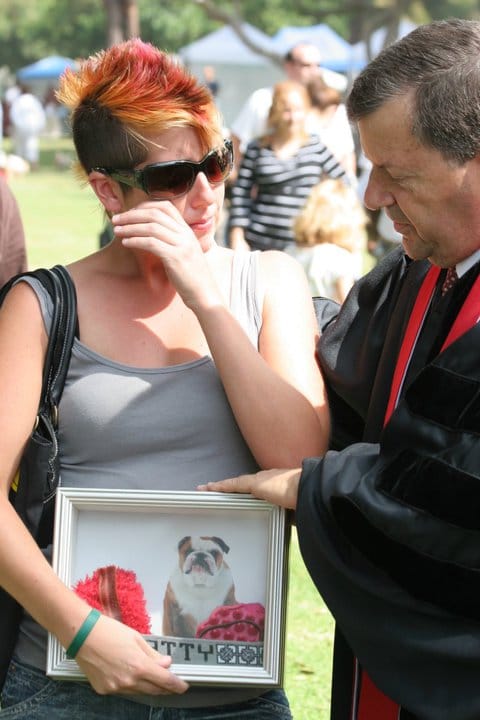 A man in a religious robe comforts a woman holding a picture of a dog.