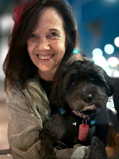 A smiling woman holding a black dog.