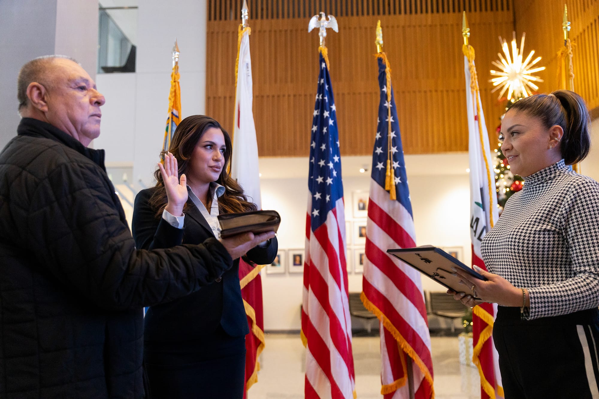 A man and two women stand in front of American and other flags.