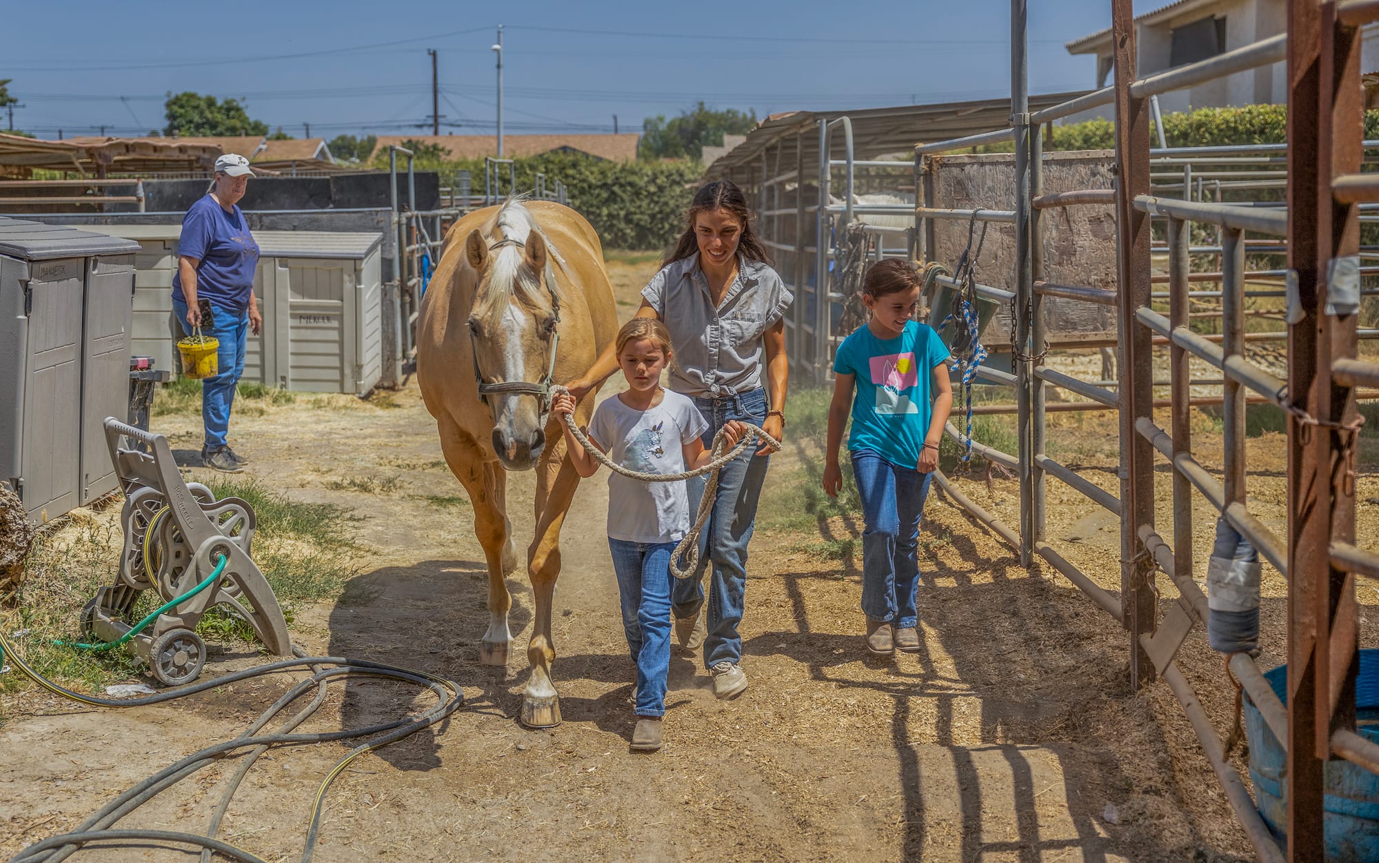 Two young girls walk with a horse accompanied by a trainer.