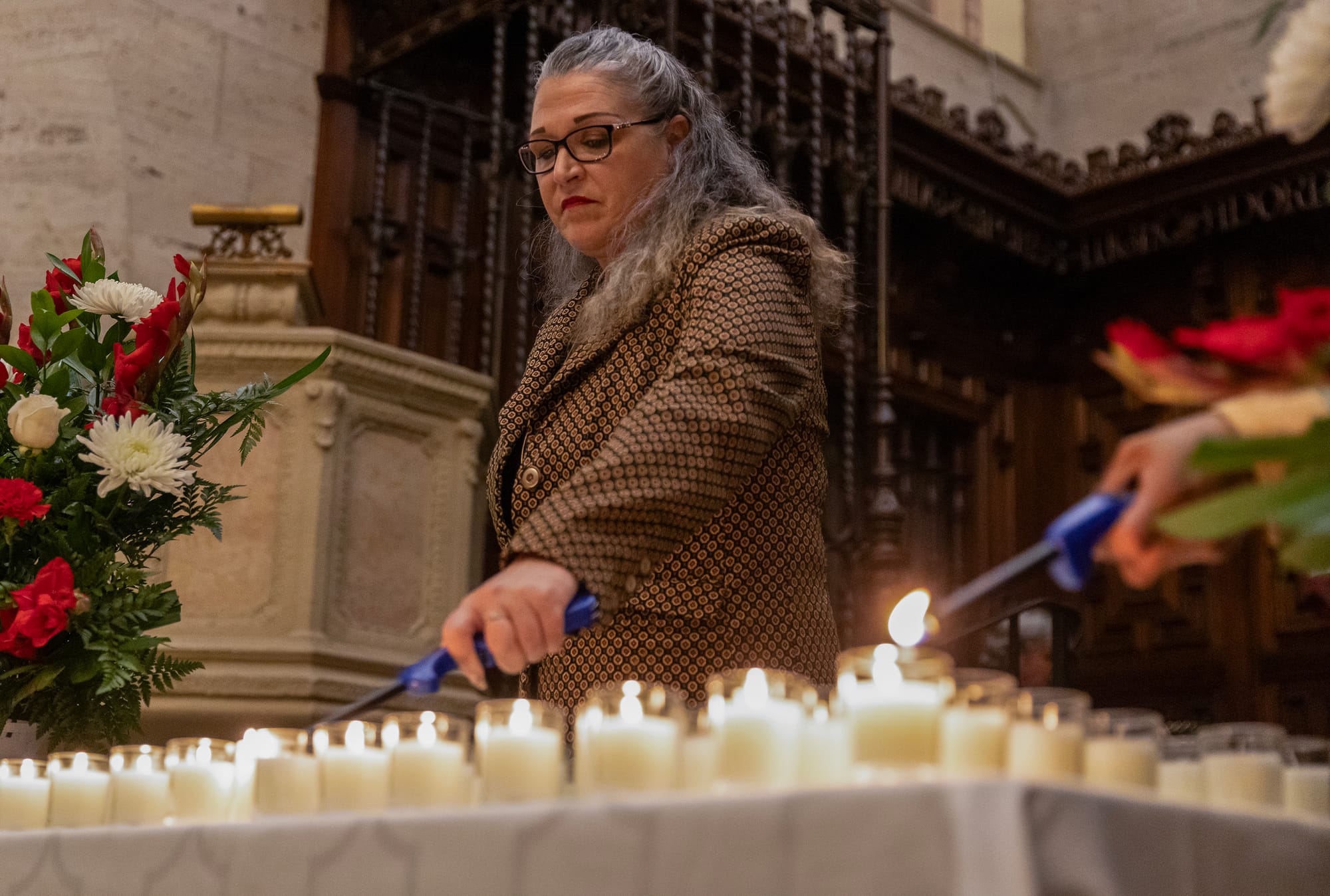 A woman lights many candles with a blue stick lighter.