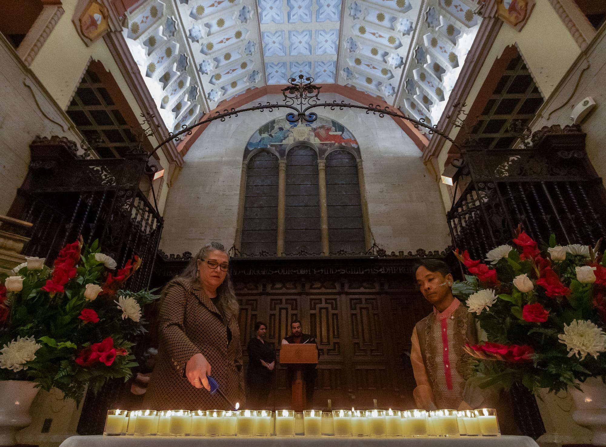 Two people light numerous candles inside a chapel.