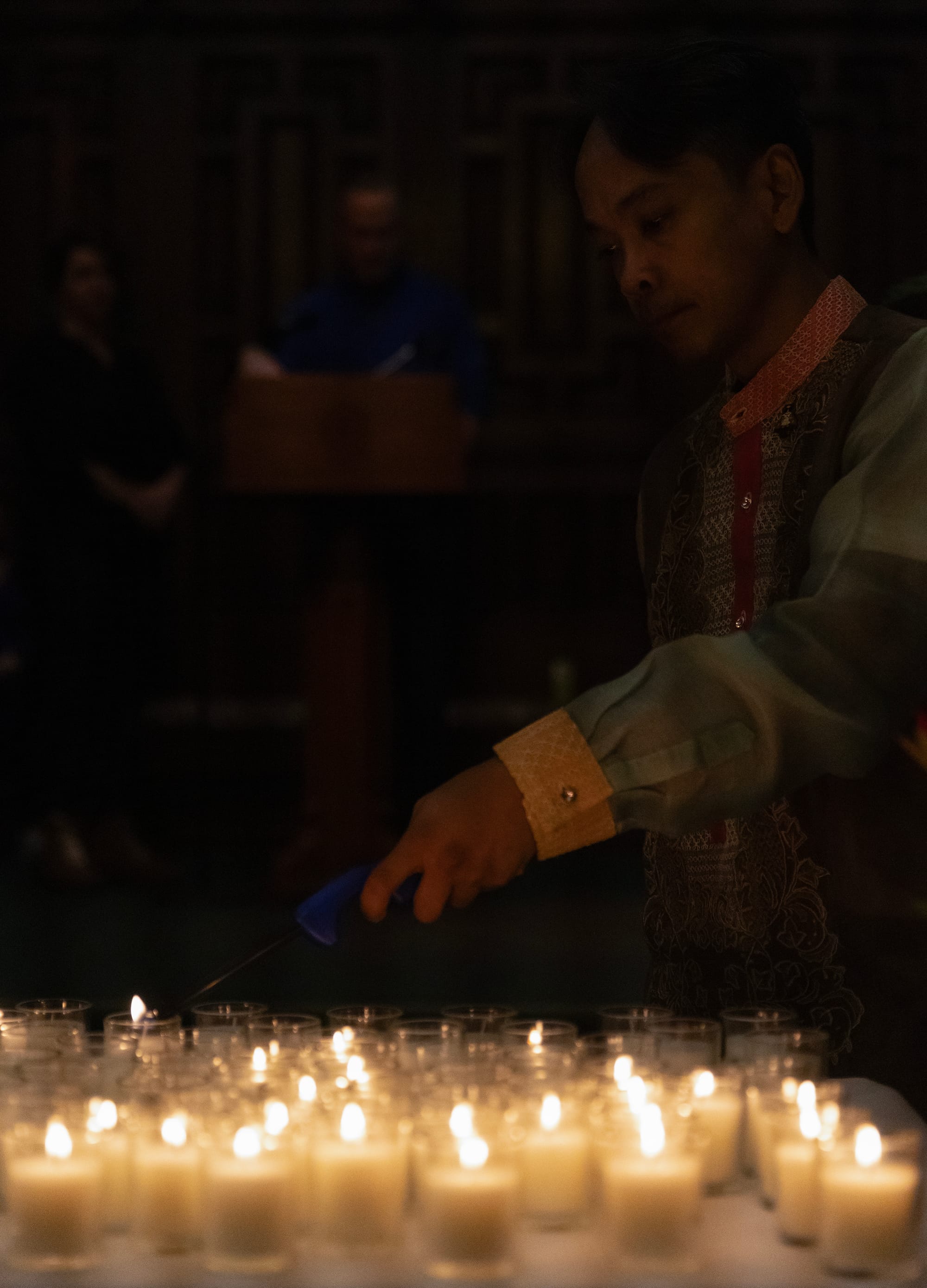 A man standing in shadow lights many candles.