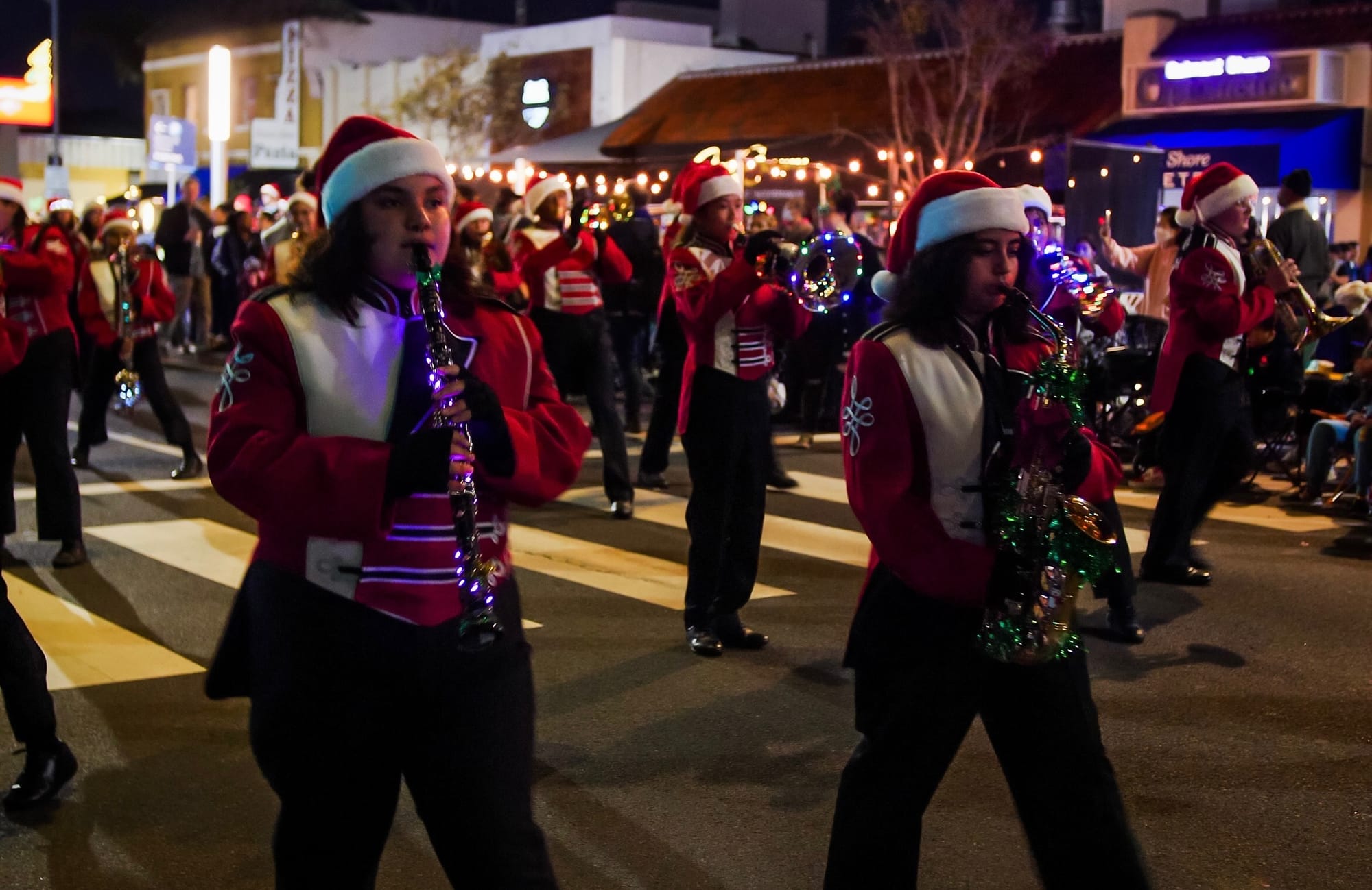 Band members wearing red uniforms play musical instruments during a nighttime parade.