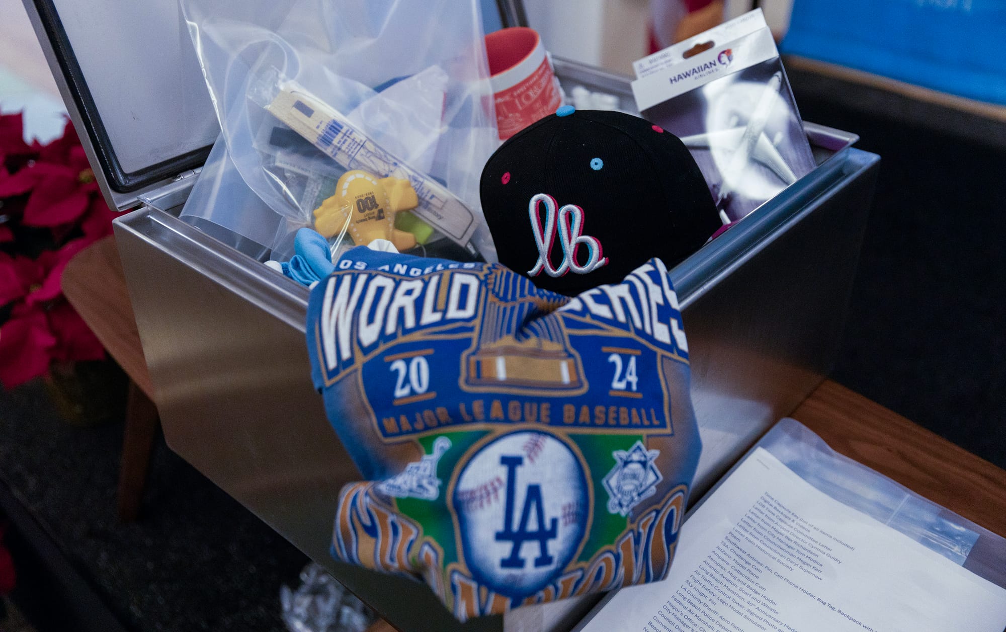 Various items, including a Dodgers shirt, a Long Beach hat and model plans sit in a silver metal box.