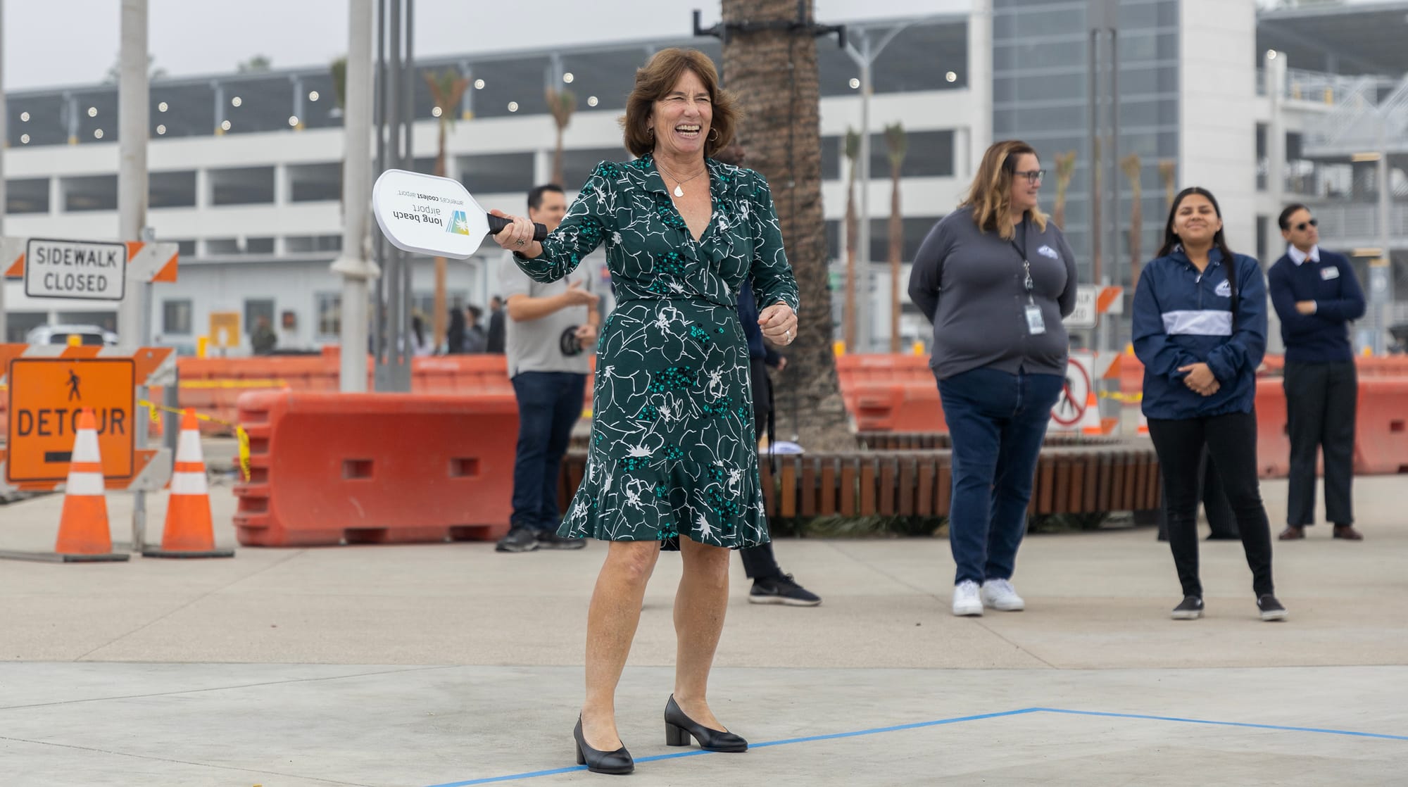 A woman in a green dress and black heels laughs and points a white paddle.