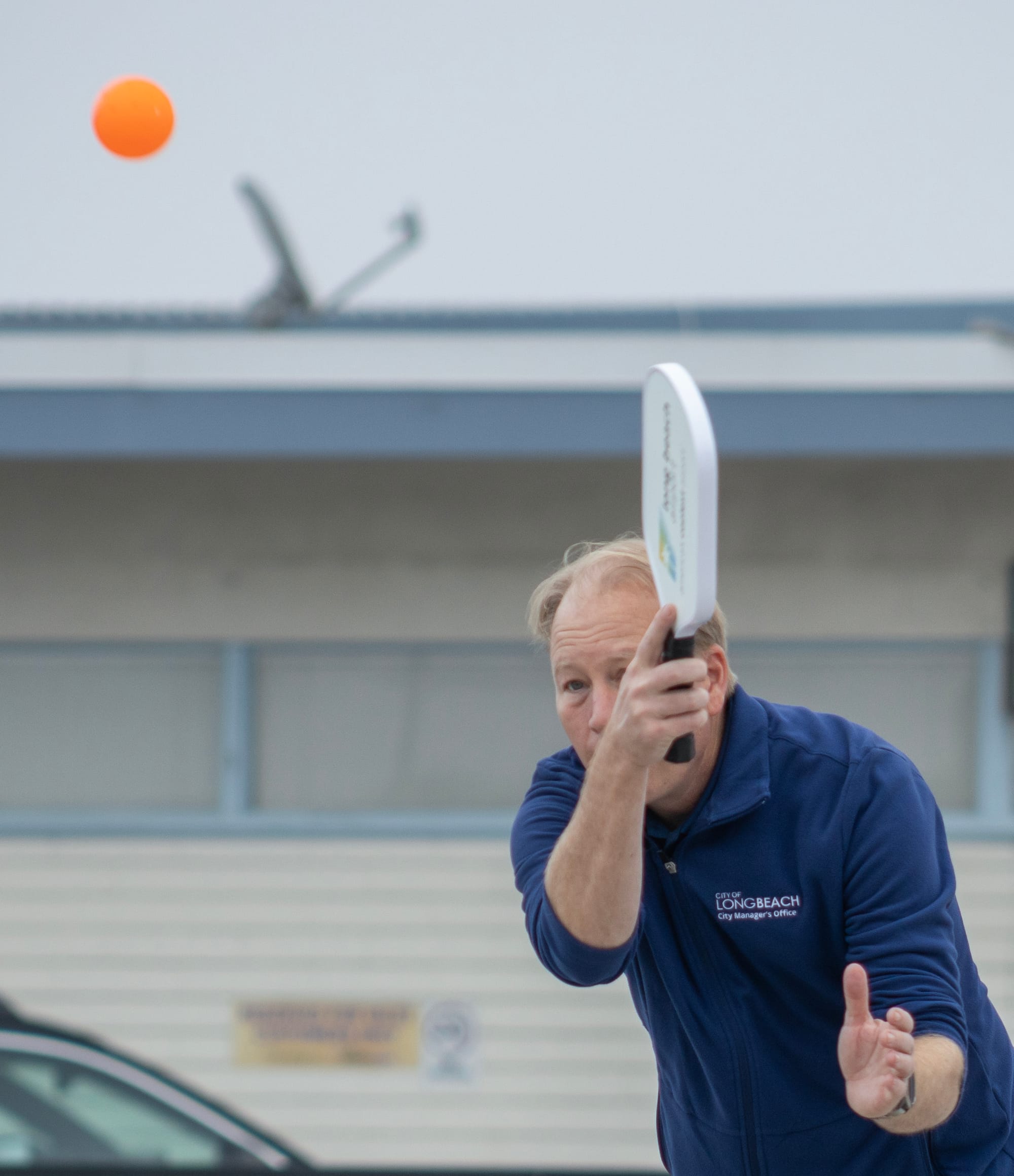 A man in a dark blue jacket swings a white paddle.