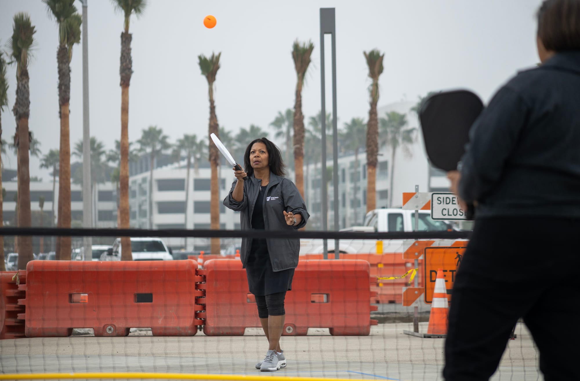 A woman hits an orange ball with a white paddle.