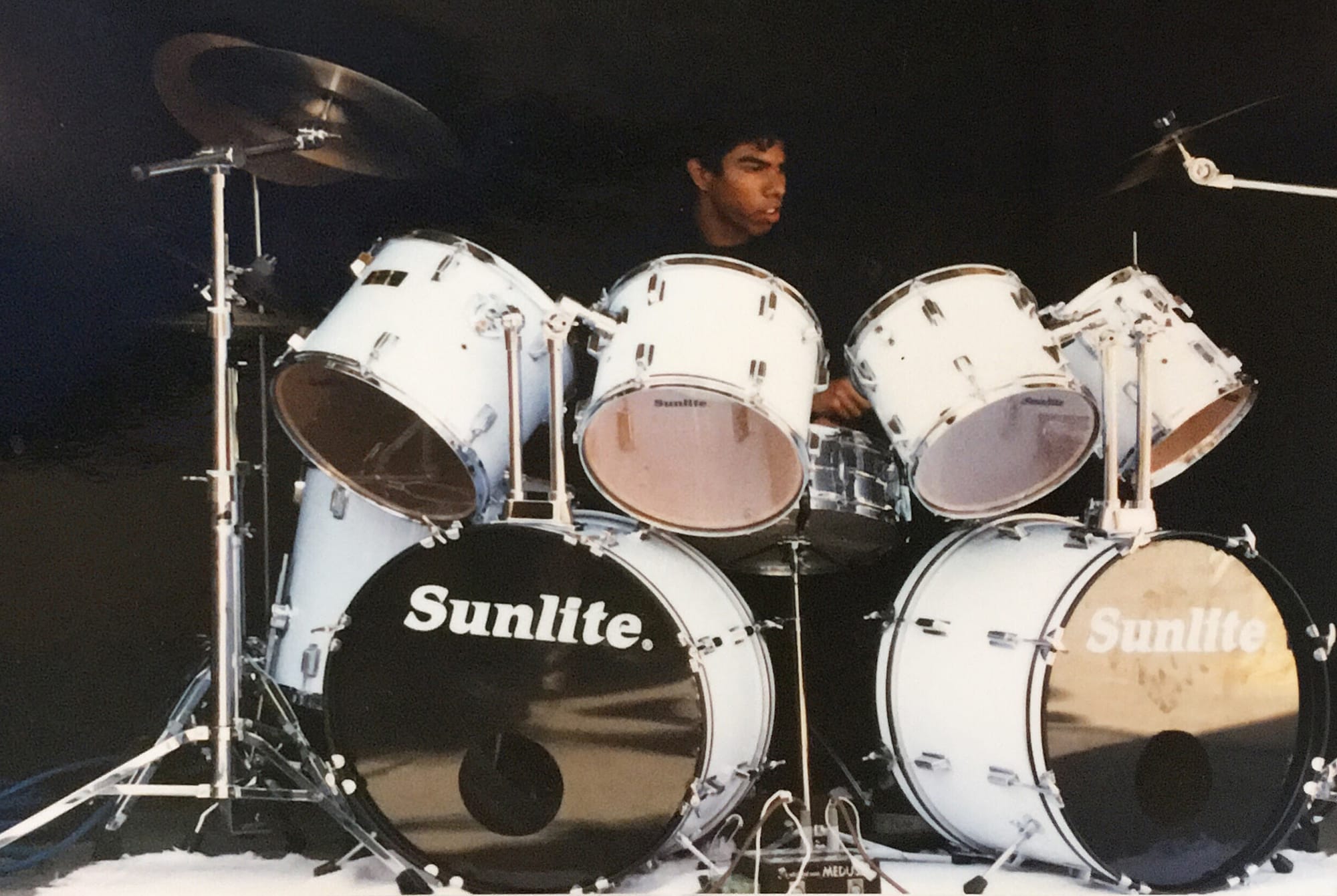 A young boy sits behind a white drum set that says "sunlite."