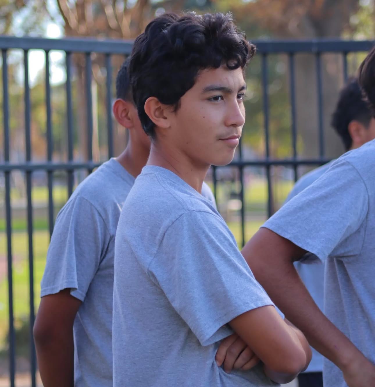 A teen boy in a gray t-shirt standing in front of other teens.