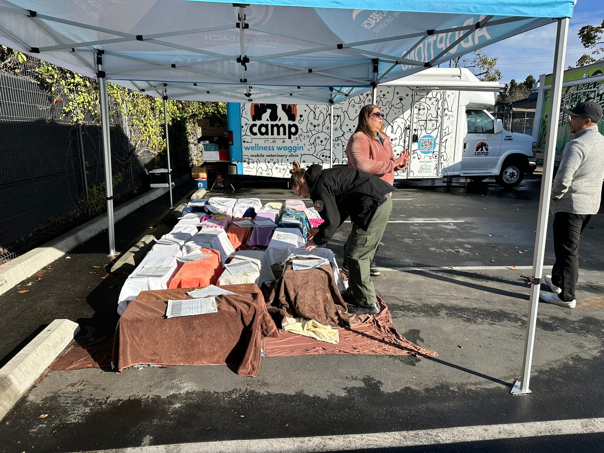 Two people stand under a canopy next to a dozen cat cages draped in towels.