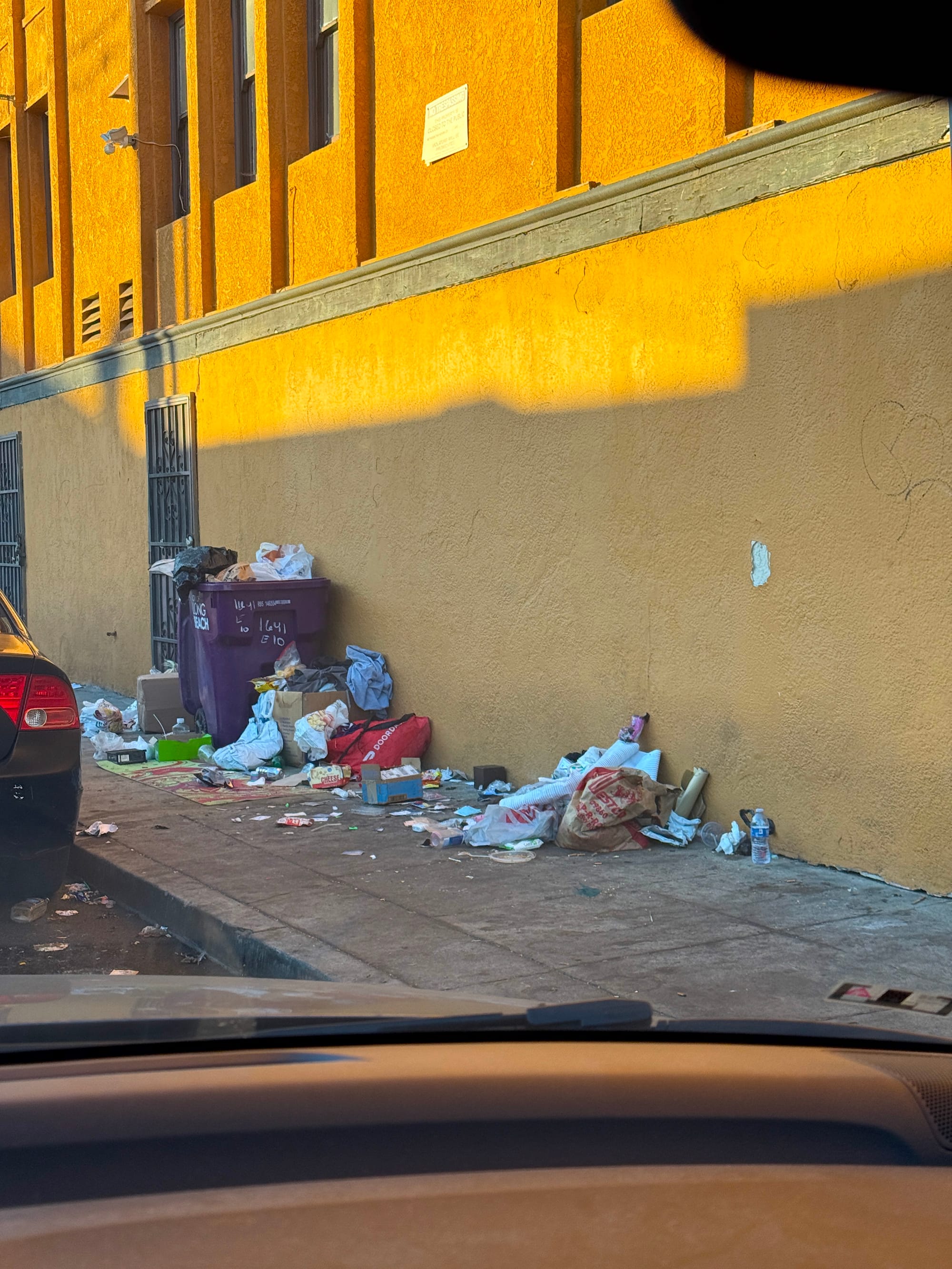 A purple garbage bin on the sidewalk overflowing with trash.