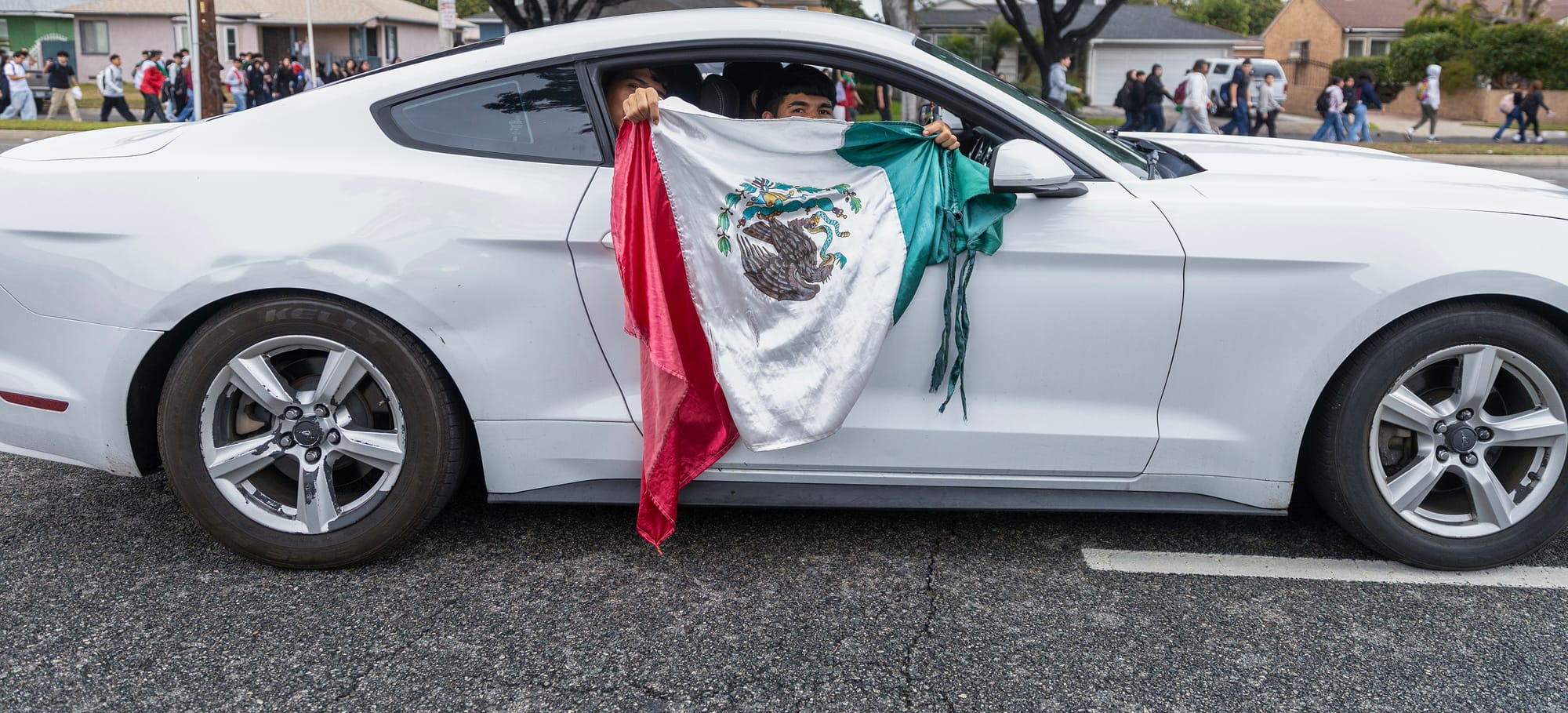 A person in a white car holds a Mexican flag out the window.