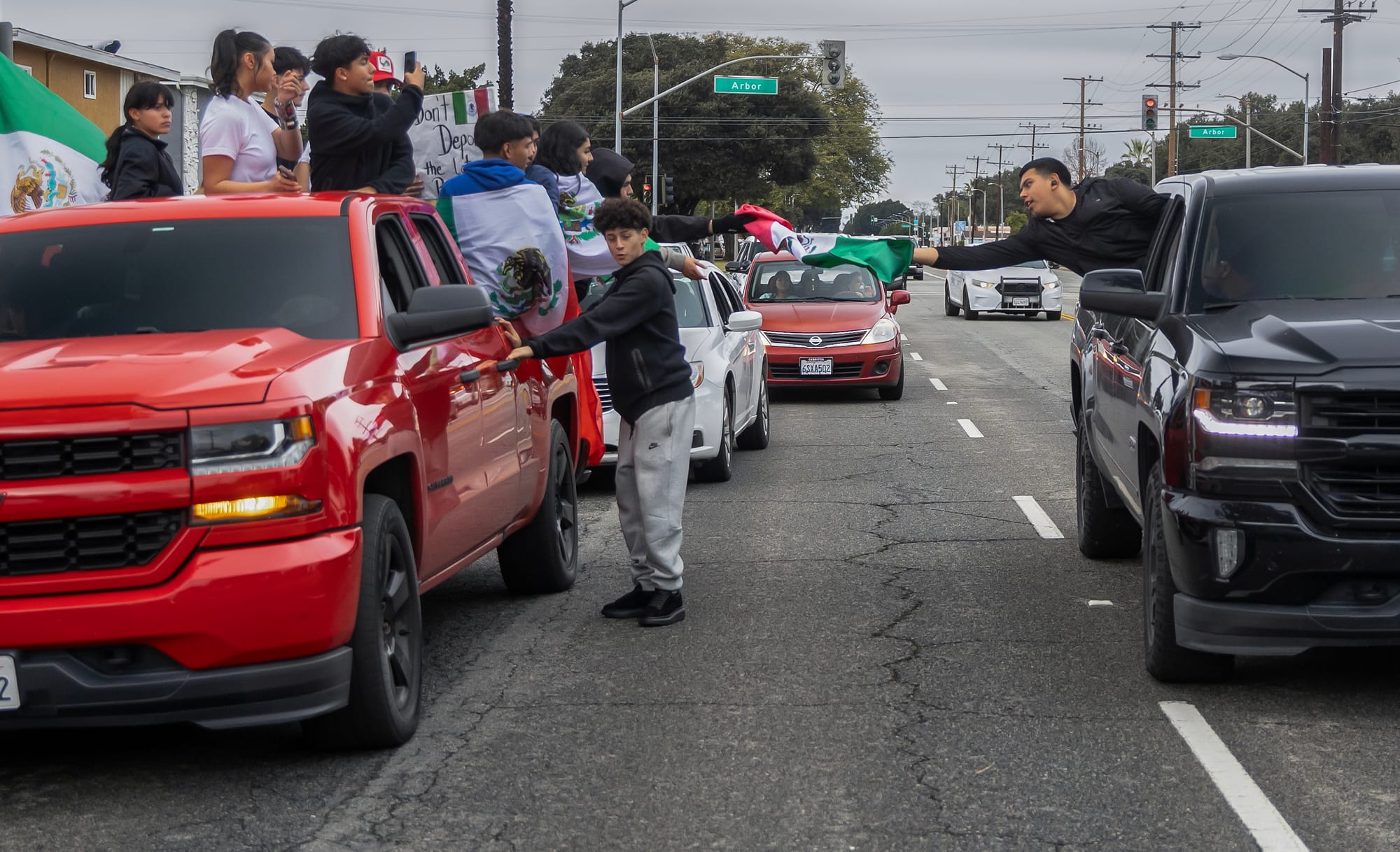 A teen holding a Mexican flag reaches out from inside a black truck.