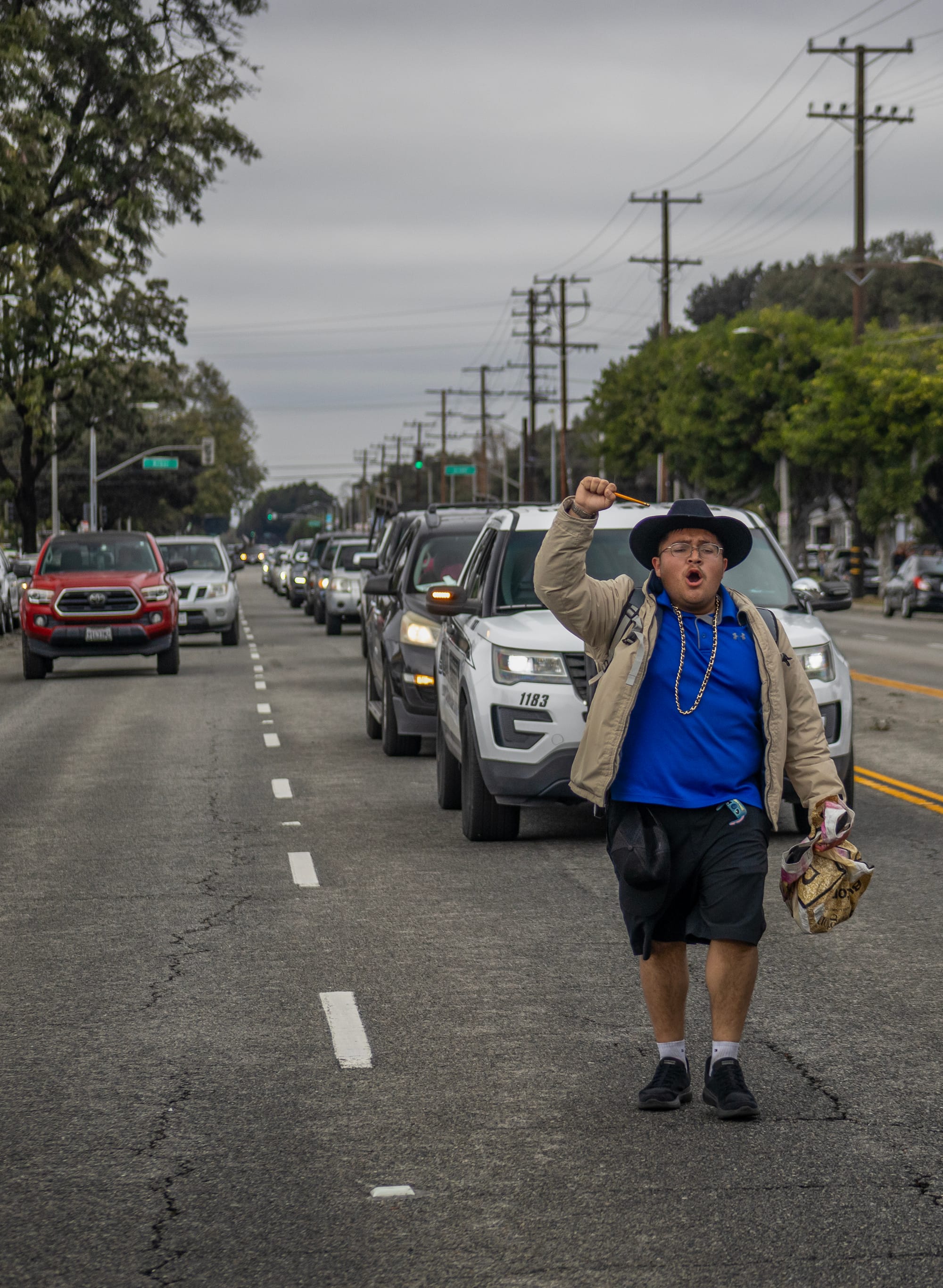 A person raises their fist as they walk in front of a police car in the middle of the street.