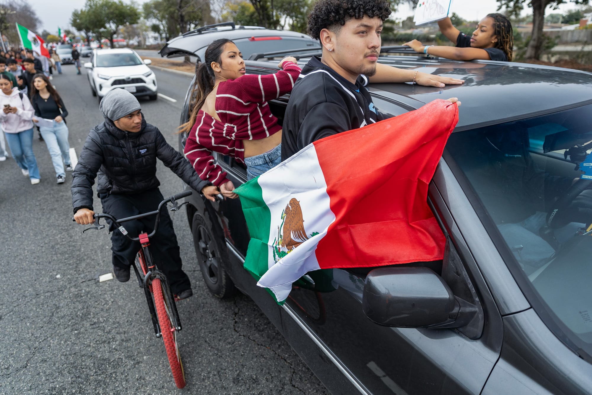 People, a bicyclist and a cars all travel down the street.