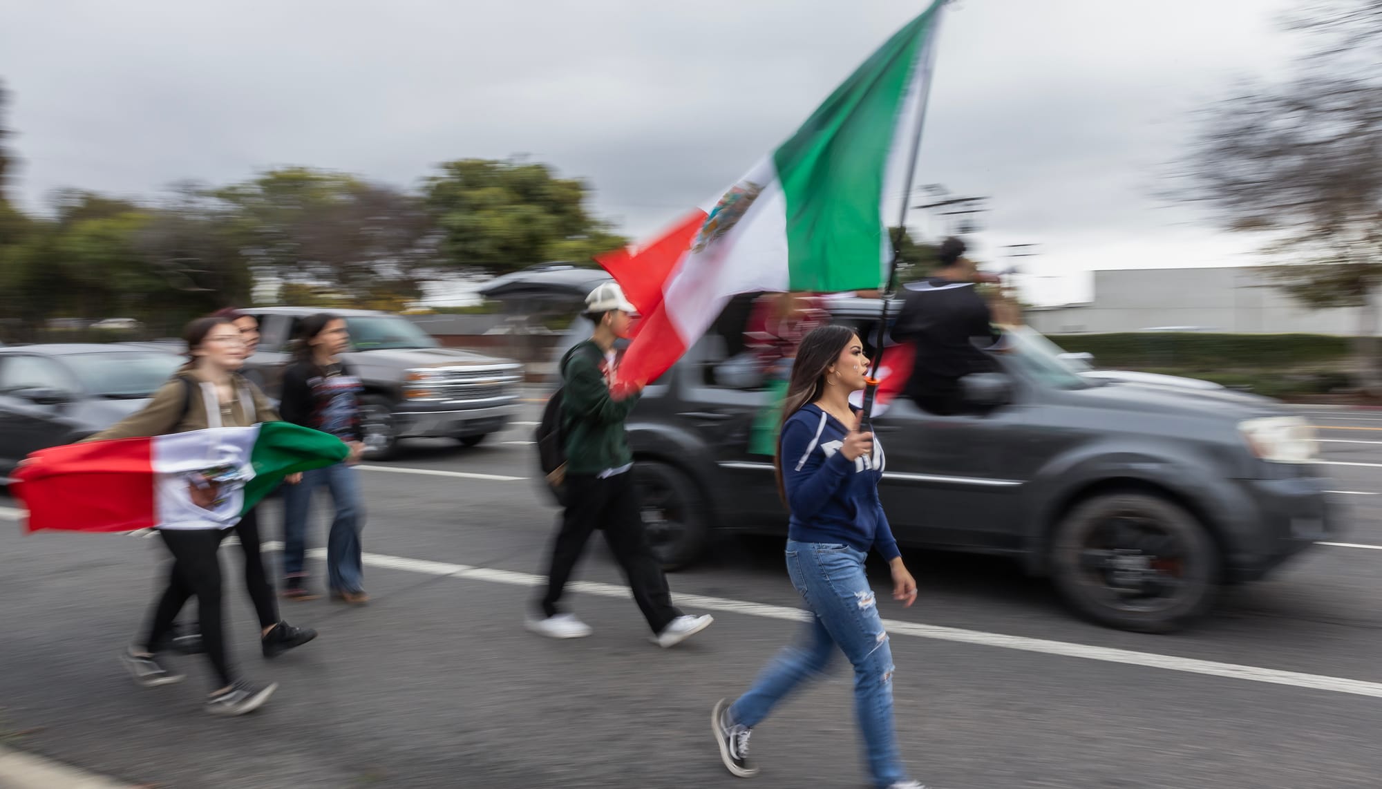 A blurry image of young people walking in the street carrying Mexican flags.