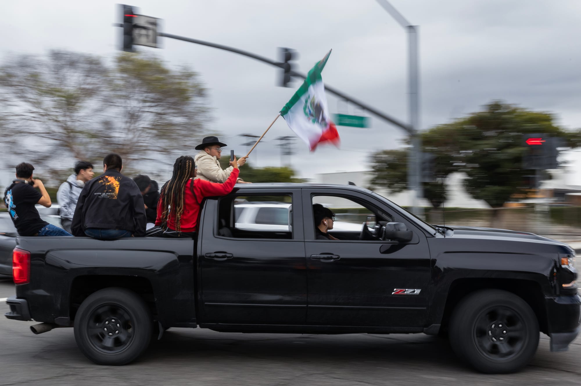 A group of people sit in the back of a black truck as it drives down the street.