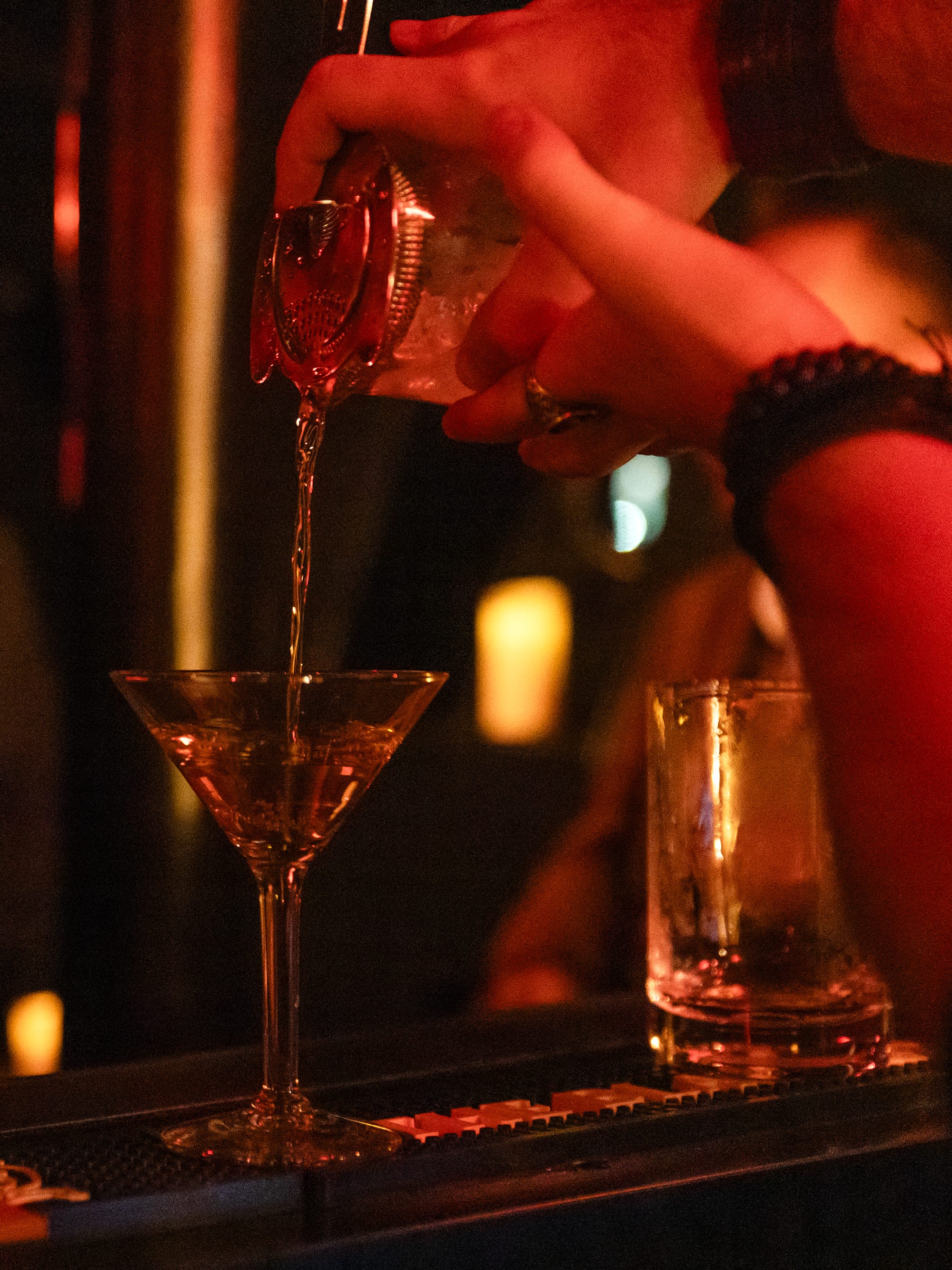 Close-up of a hand pouring liquid into a martini glass.