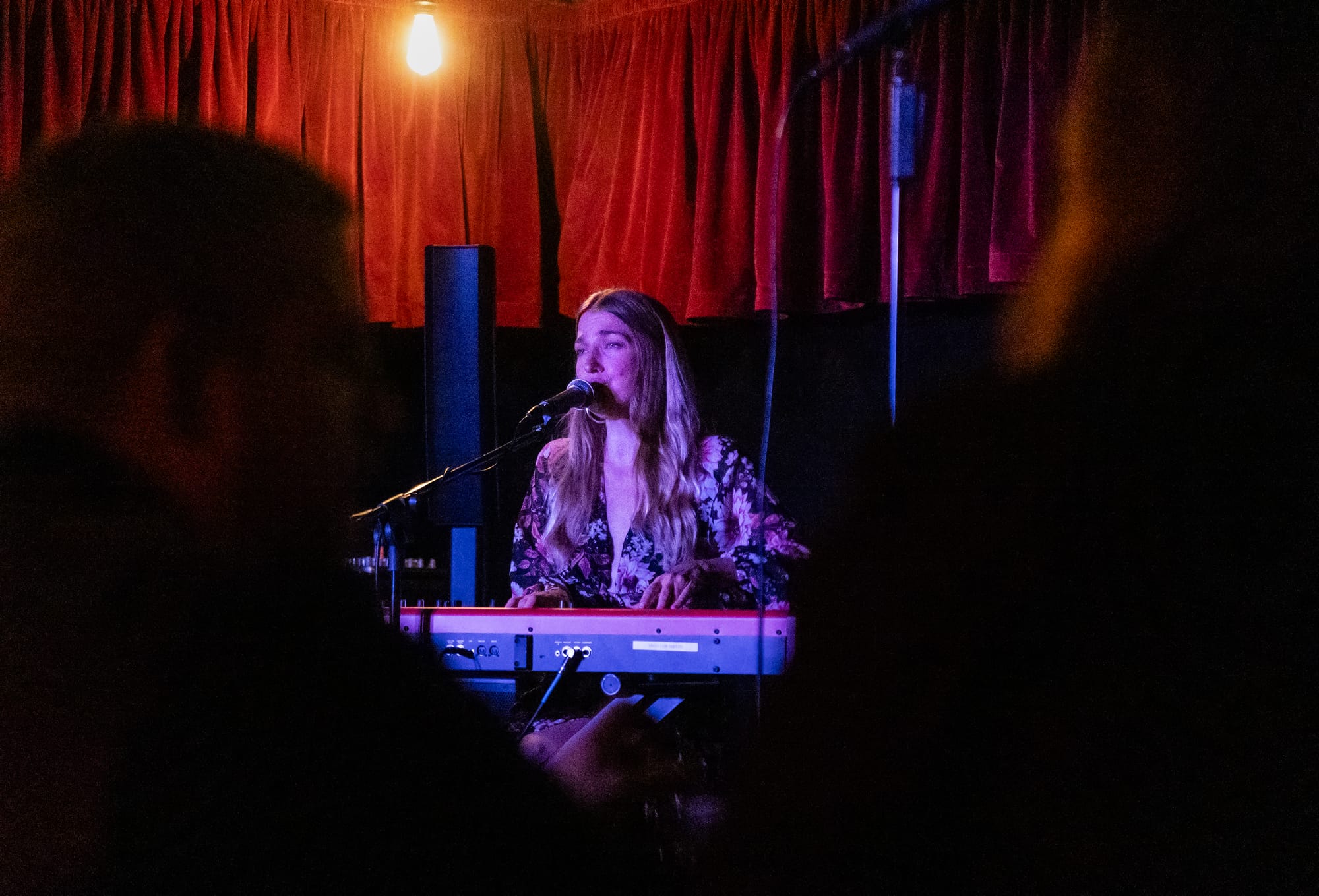 A woman sits at keyboard and speaks into a microphone.