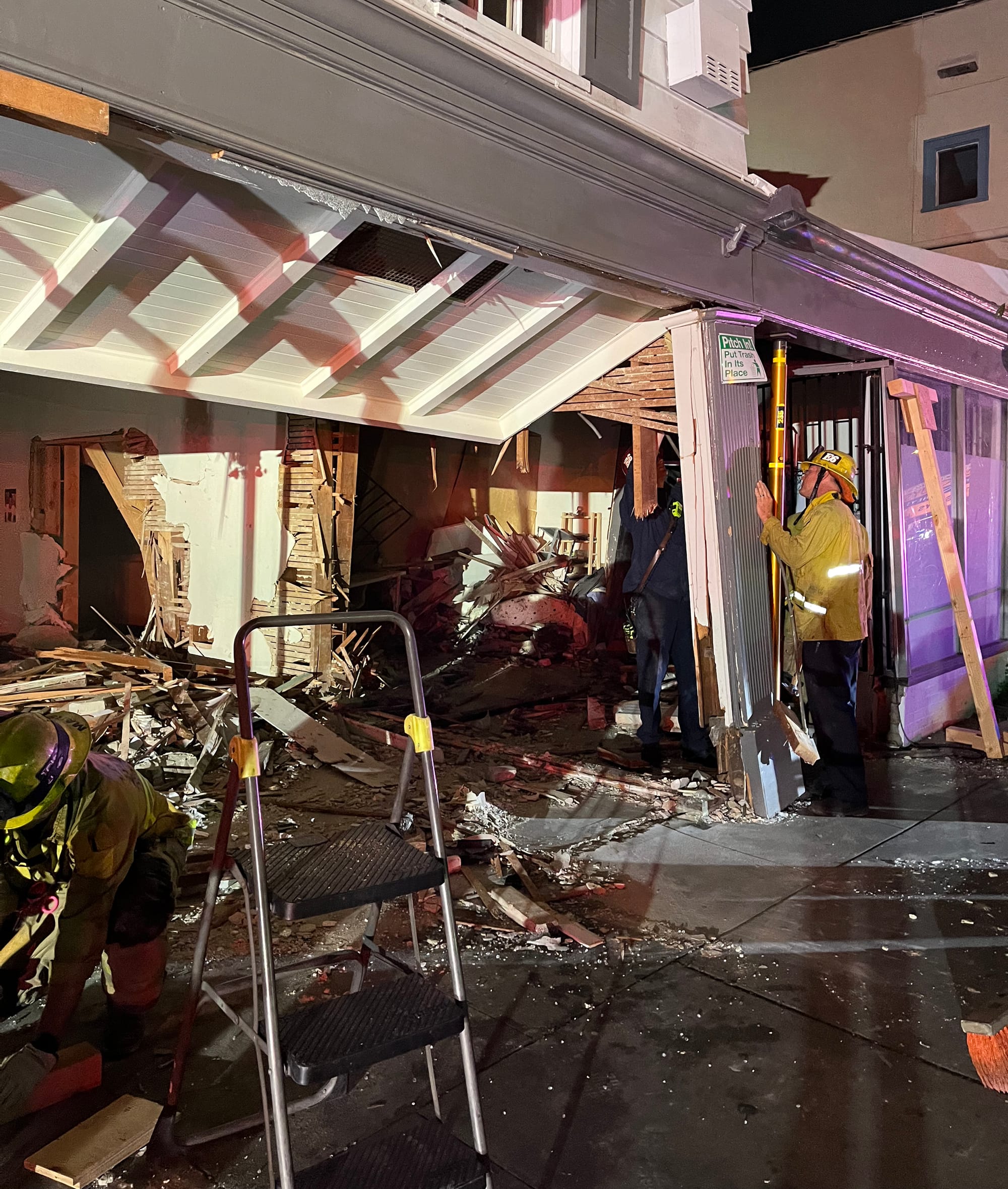 A fire fighter in a yellow jacket and helmet inspects extensive damage to a building.