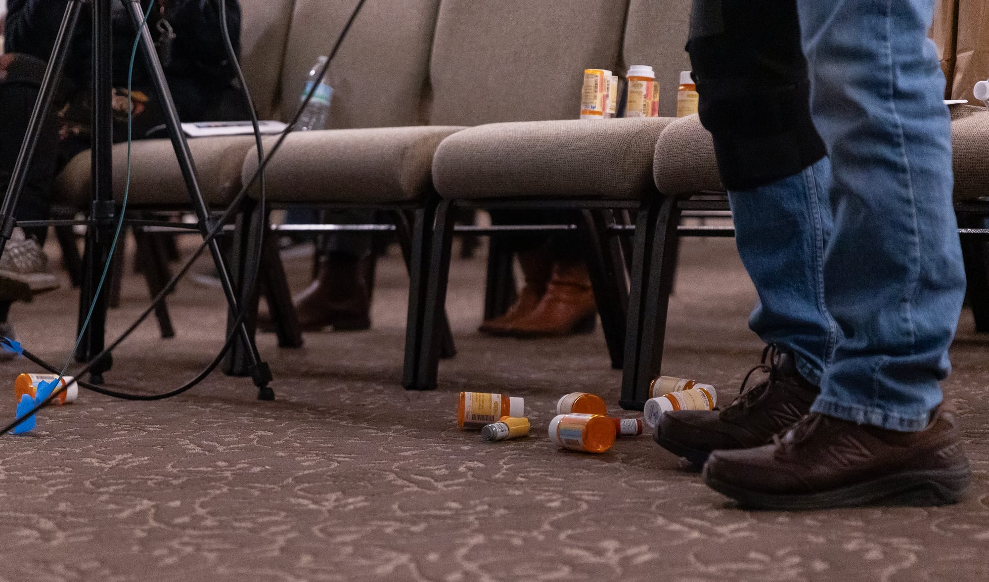 A man stands next to a half dozen prescription medication bottles lying on the floor.