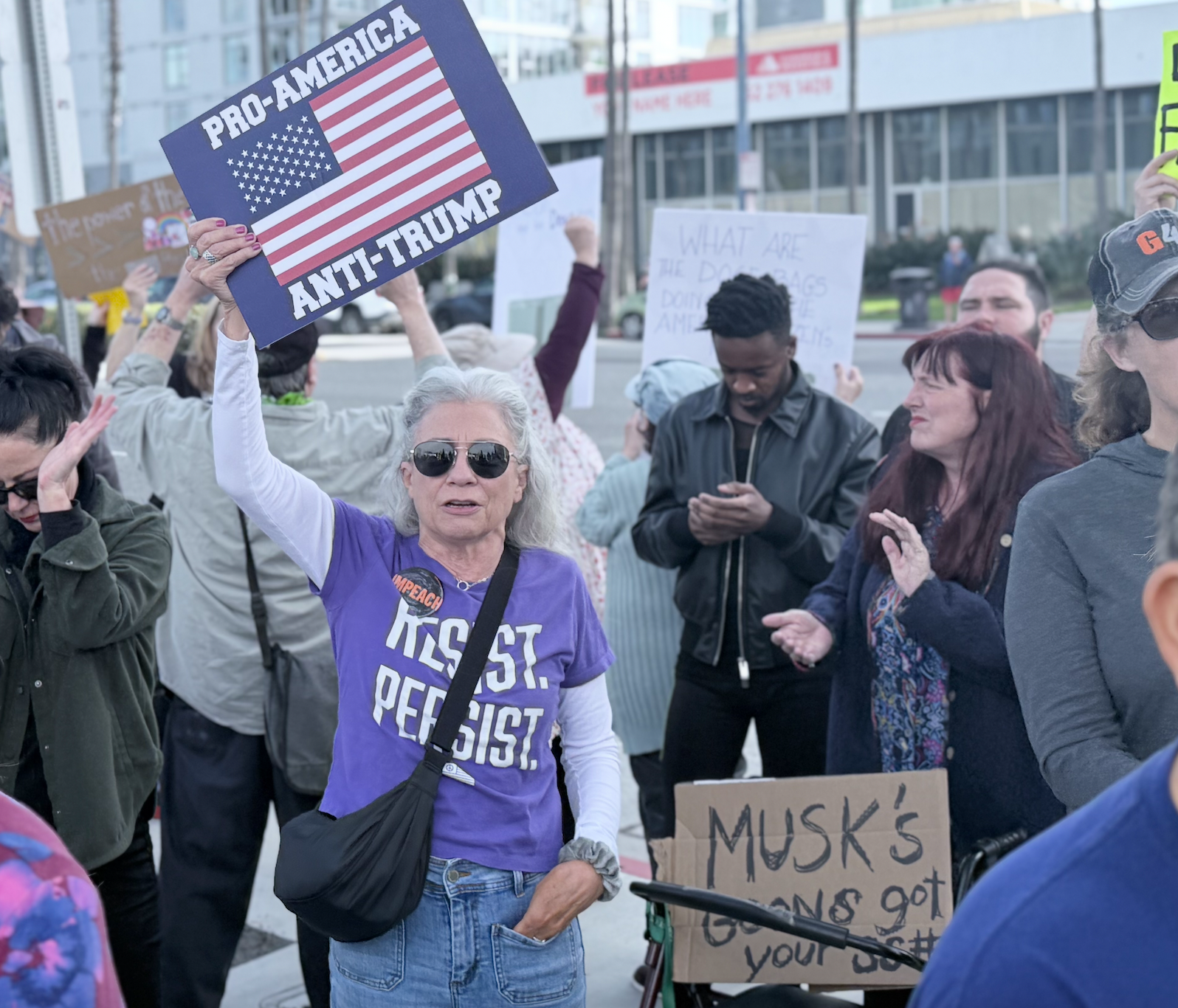 A woman stands in a group of people while holding a sign saying "Pro-America Anti-Trump."