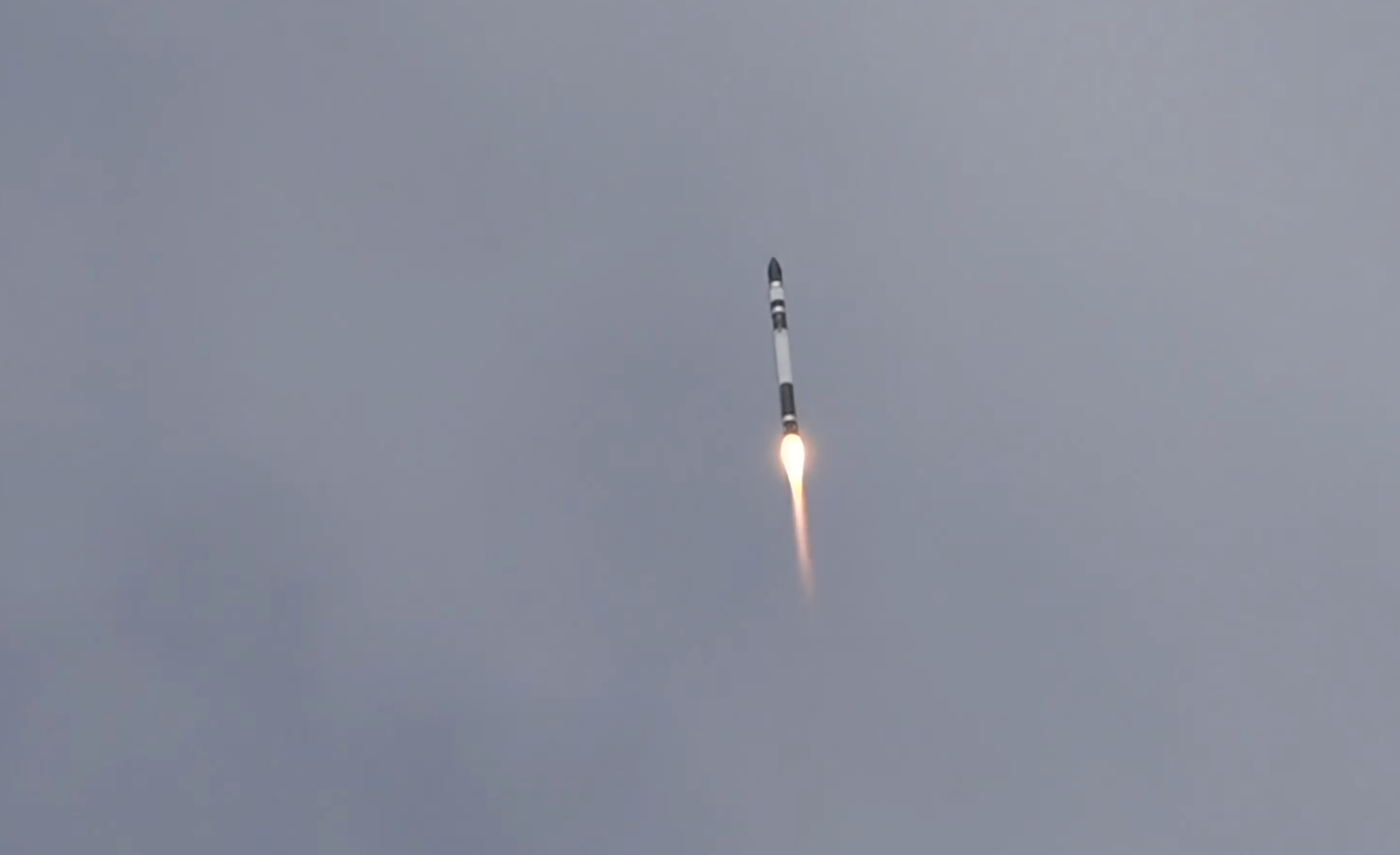 A black and white rocket flies through the air with an orange trail.