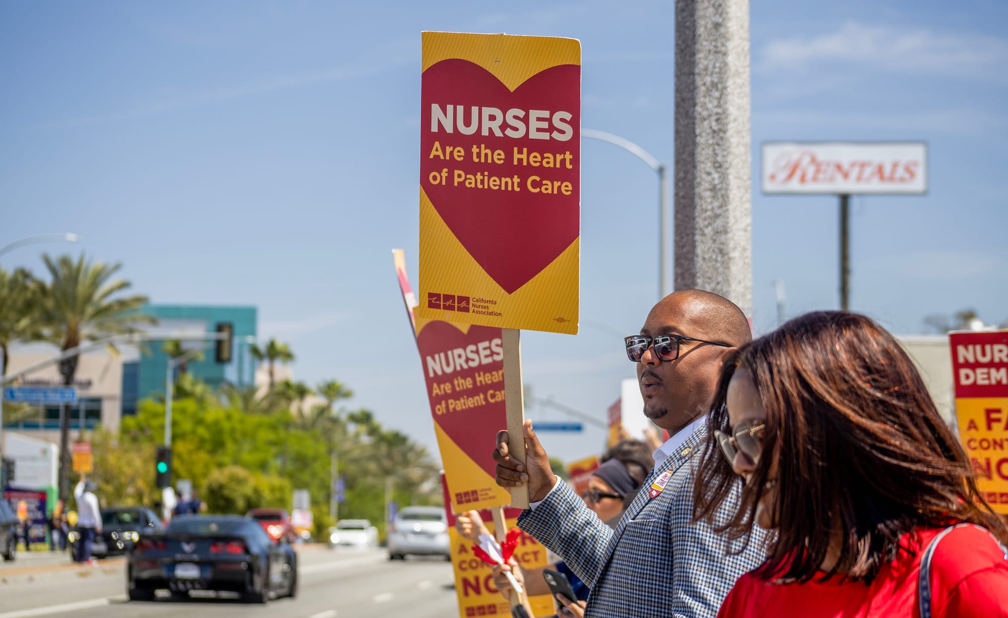 People stand on the street holding signs saying "Nurses are the heart of patient care."